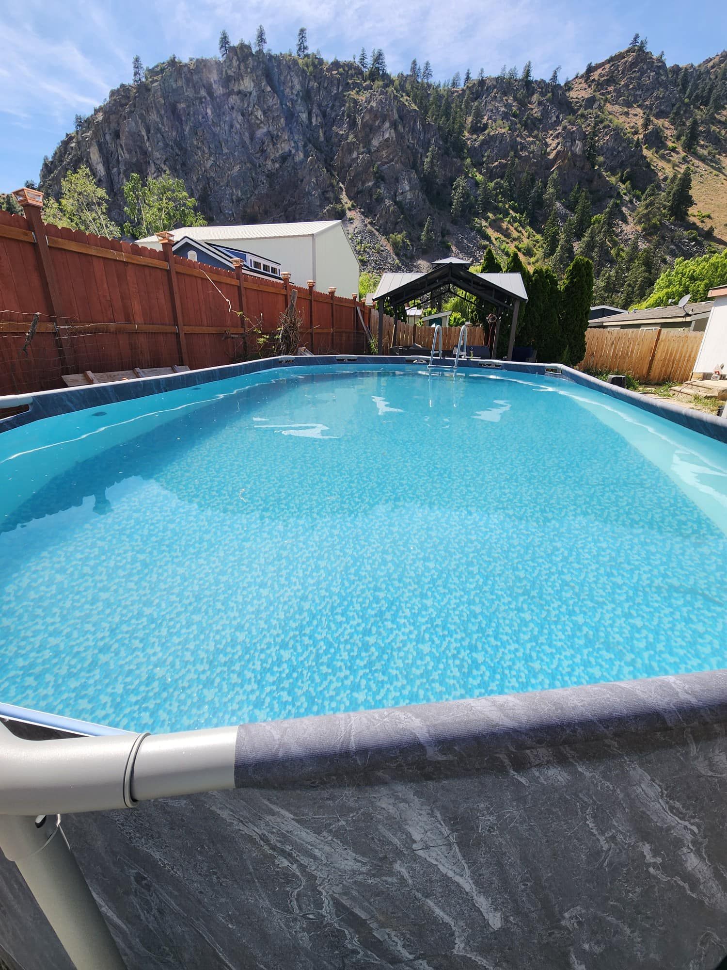 Rectangular above-ground pool in a backyard with a mountain backdrop and gazebo.