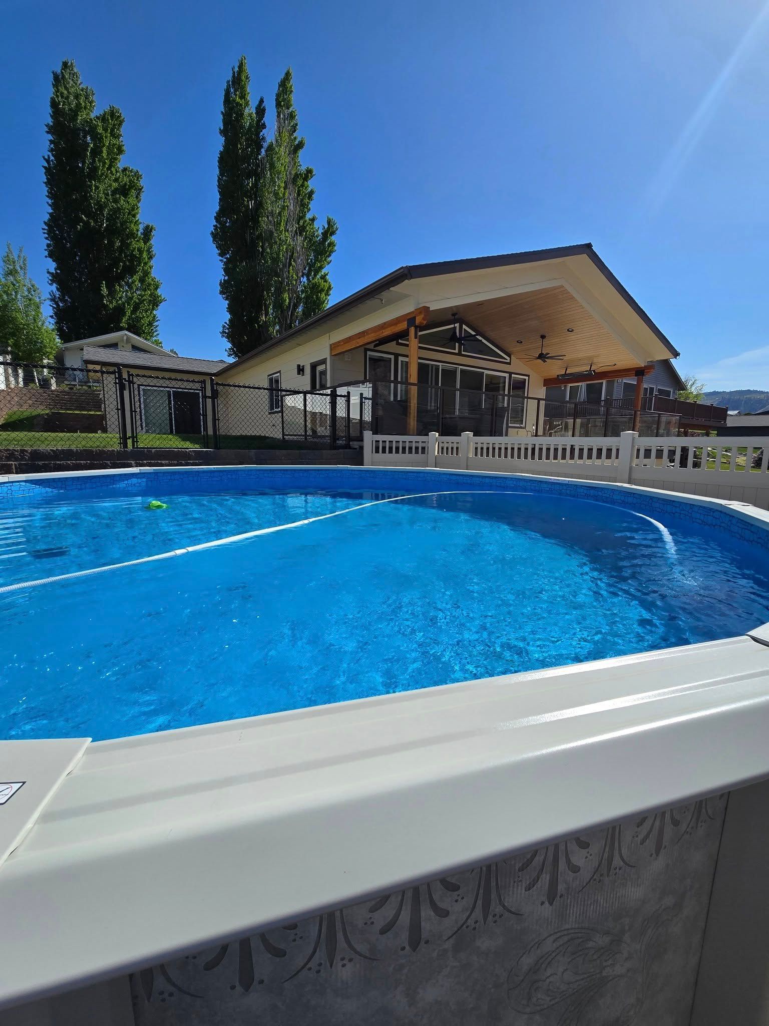 Blue pool with a covered patio and house on a sunny day.