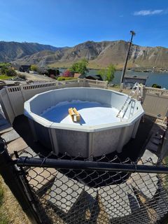 Above-ground pool being assembled with a scenic mountain and lake backdrop.