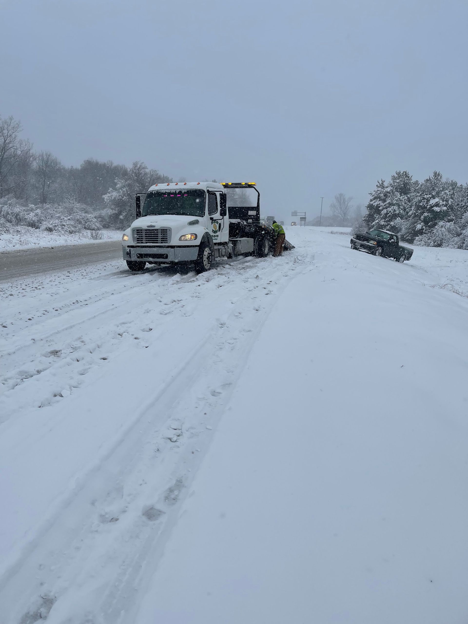 A tow truck is parked on the side of a snow covered road.