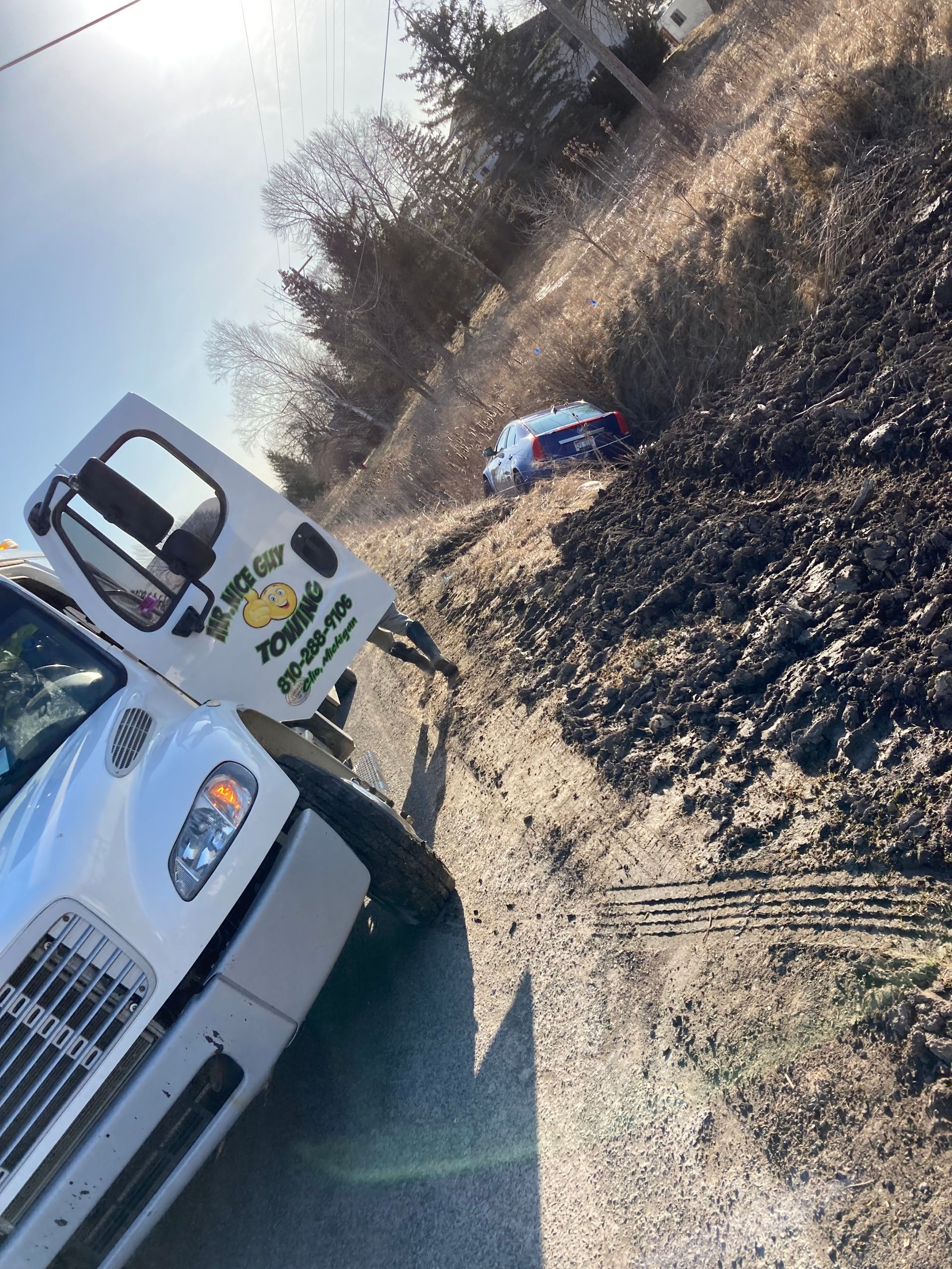 A white truck is stuck in the mud on the side of the road.