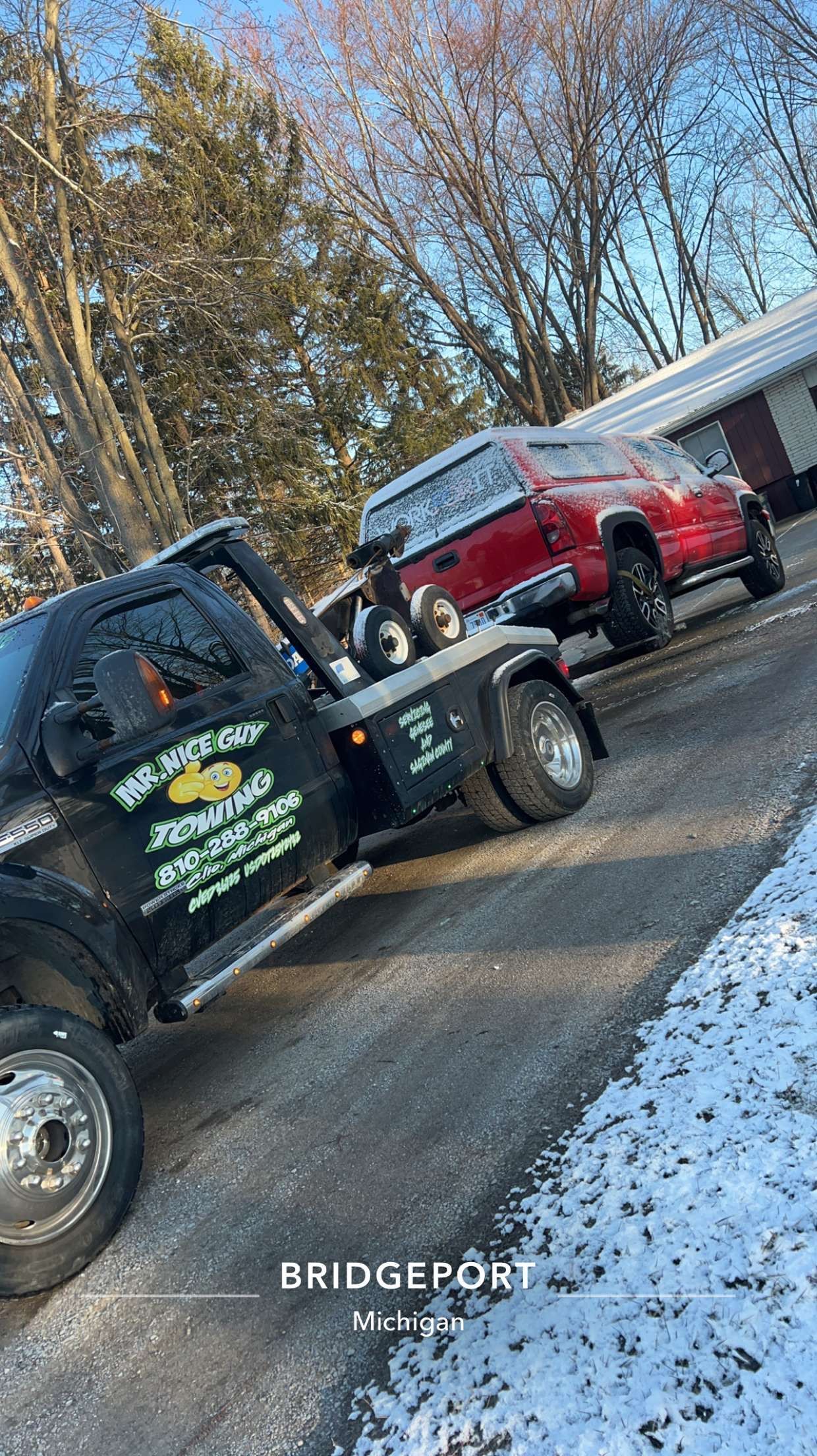 A tow truck is towing a red suv down a snowy road.