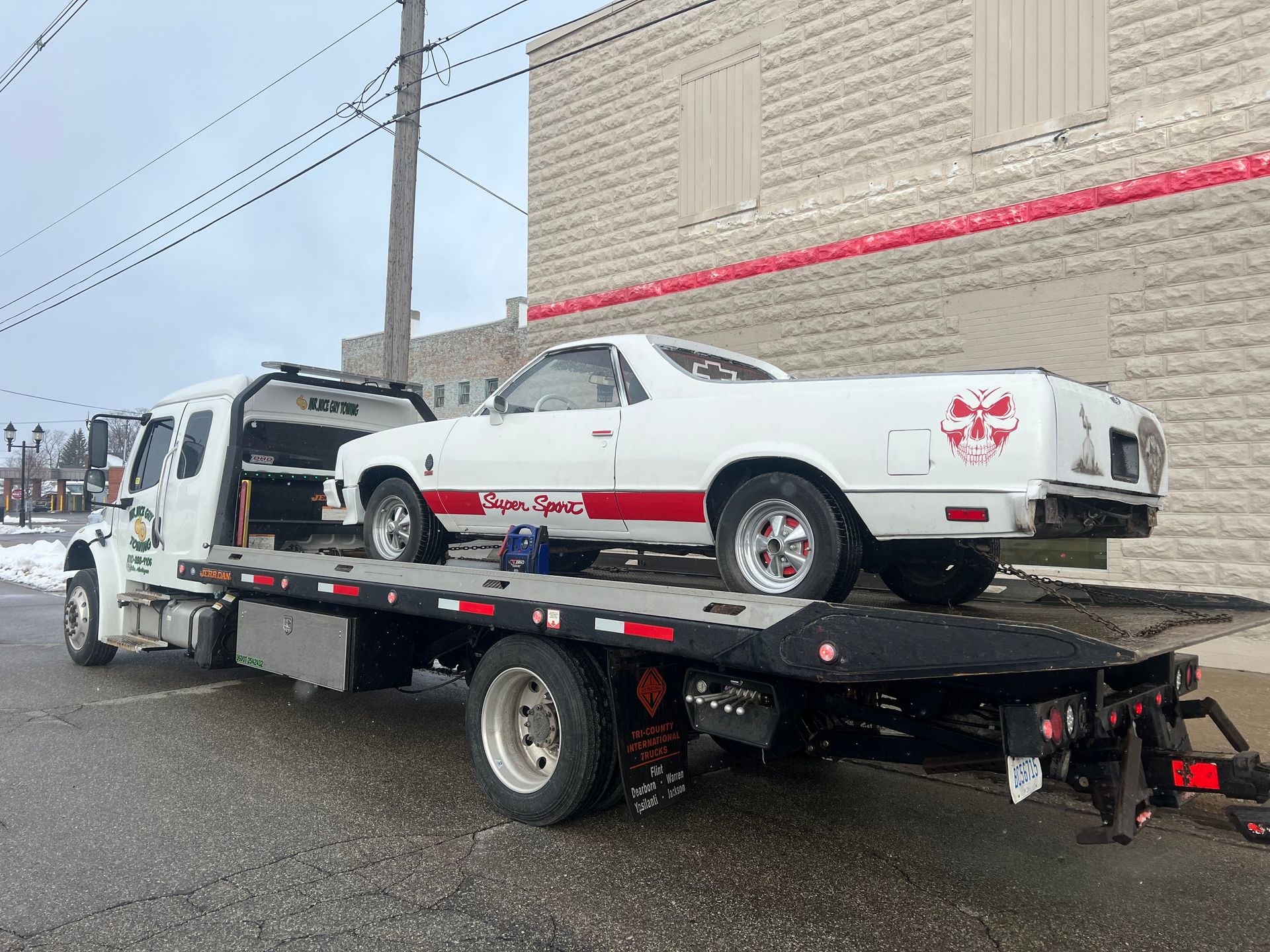 A white car is being towed by a tow truck.