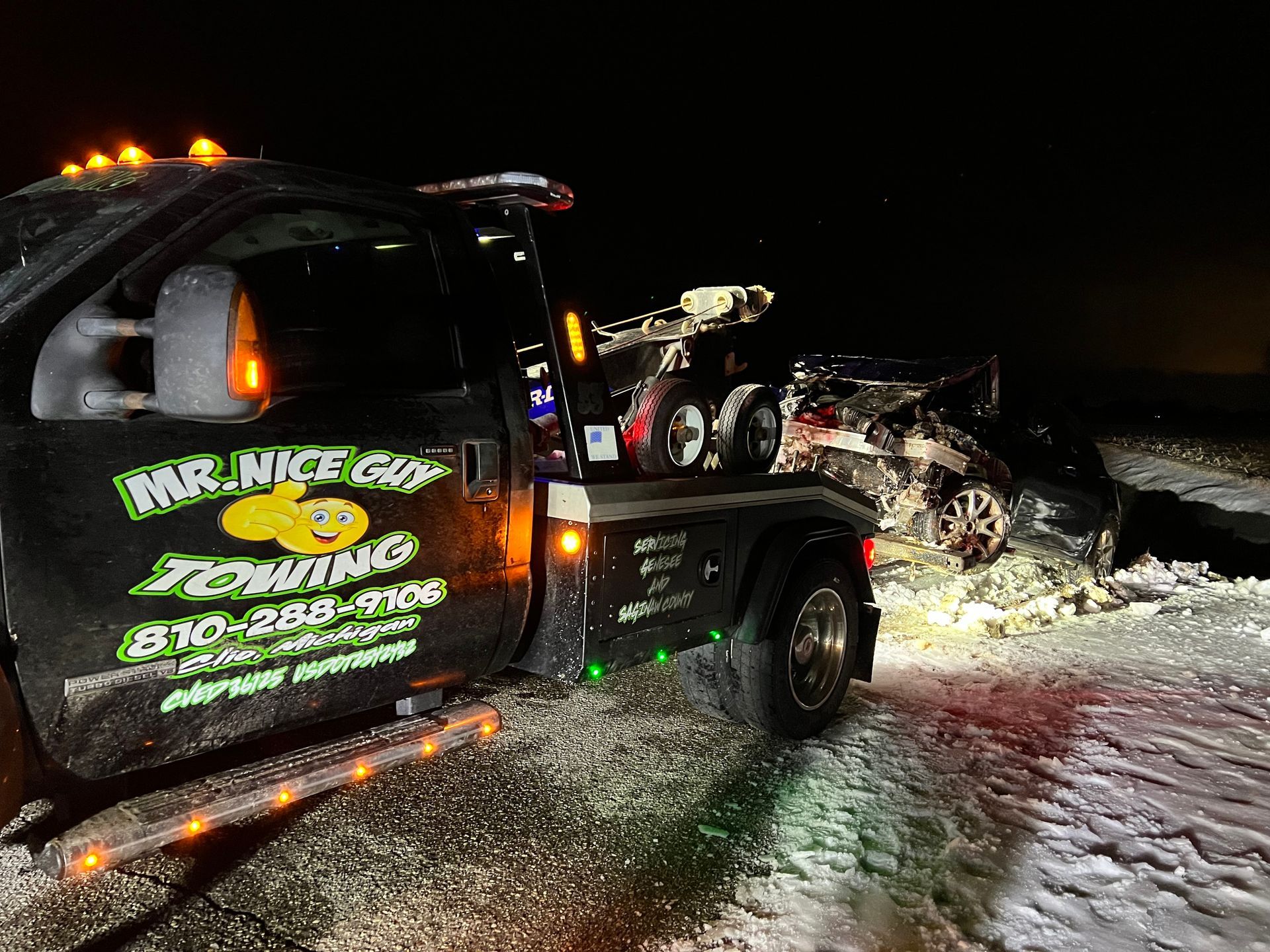 A tow truck is towing a car in the snow at night.