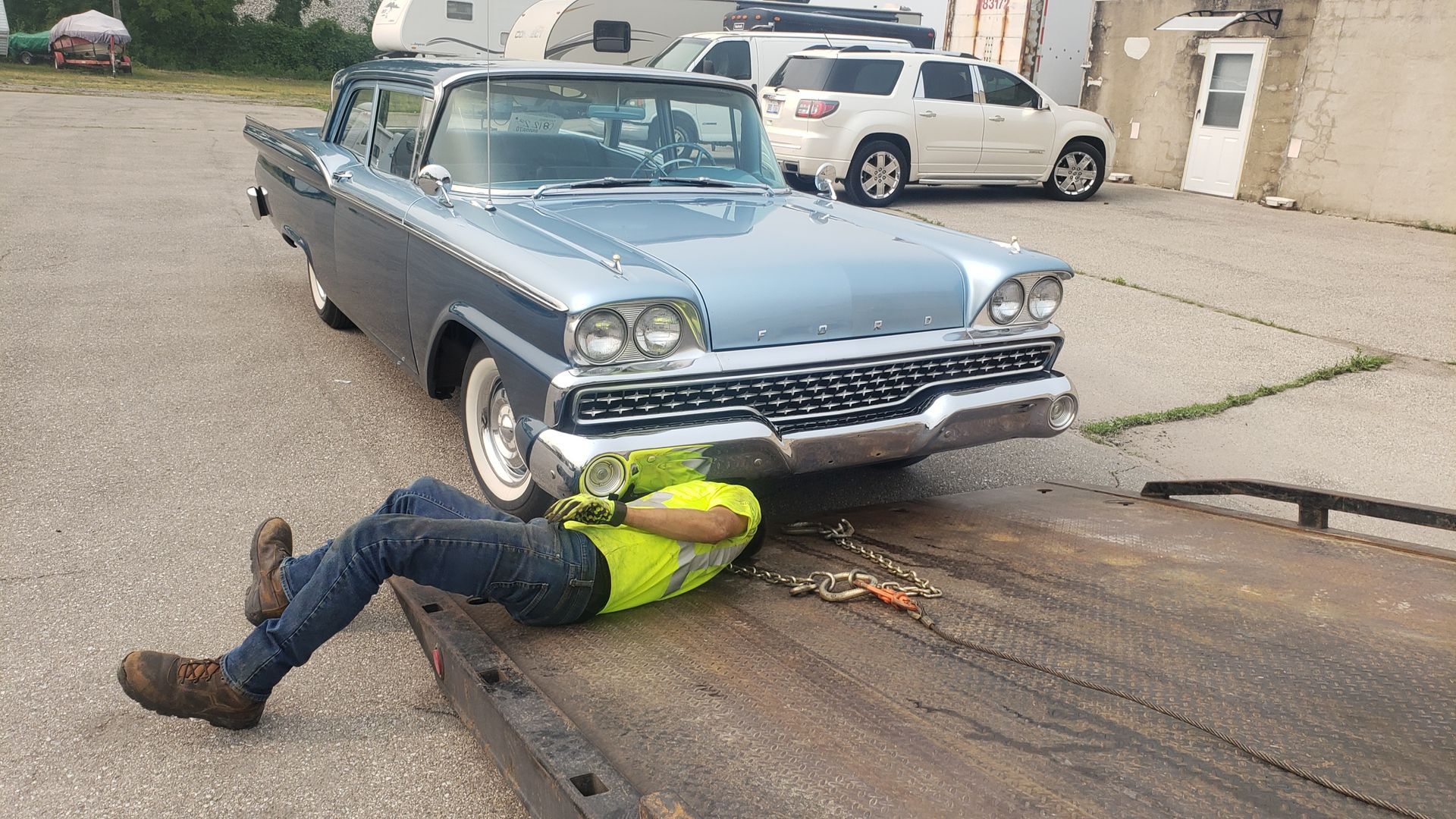 A man is laying on the ground next to a car on a tow truck.