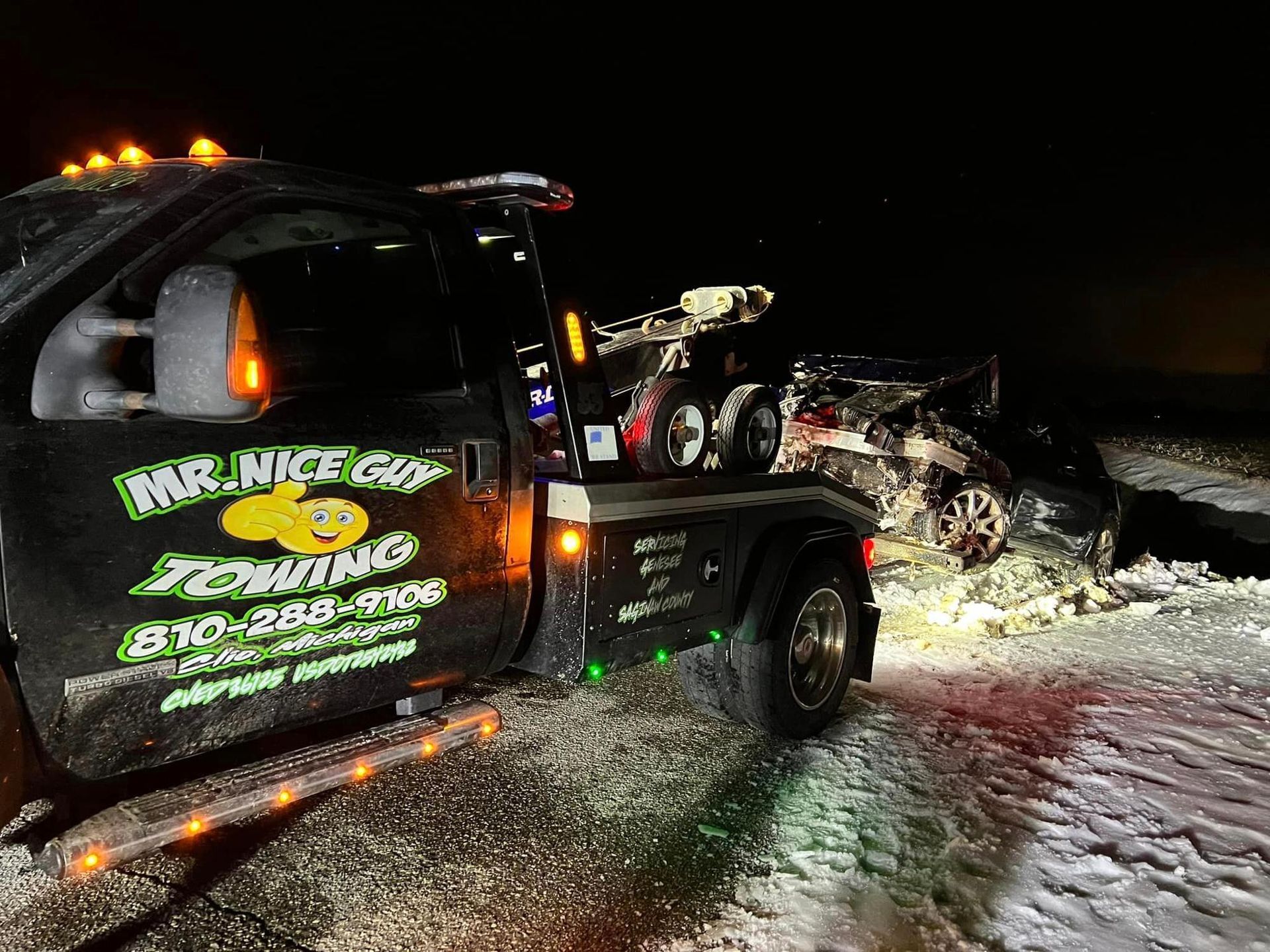 A tow truck is towing a car in the snow.