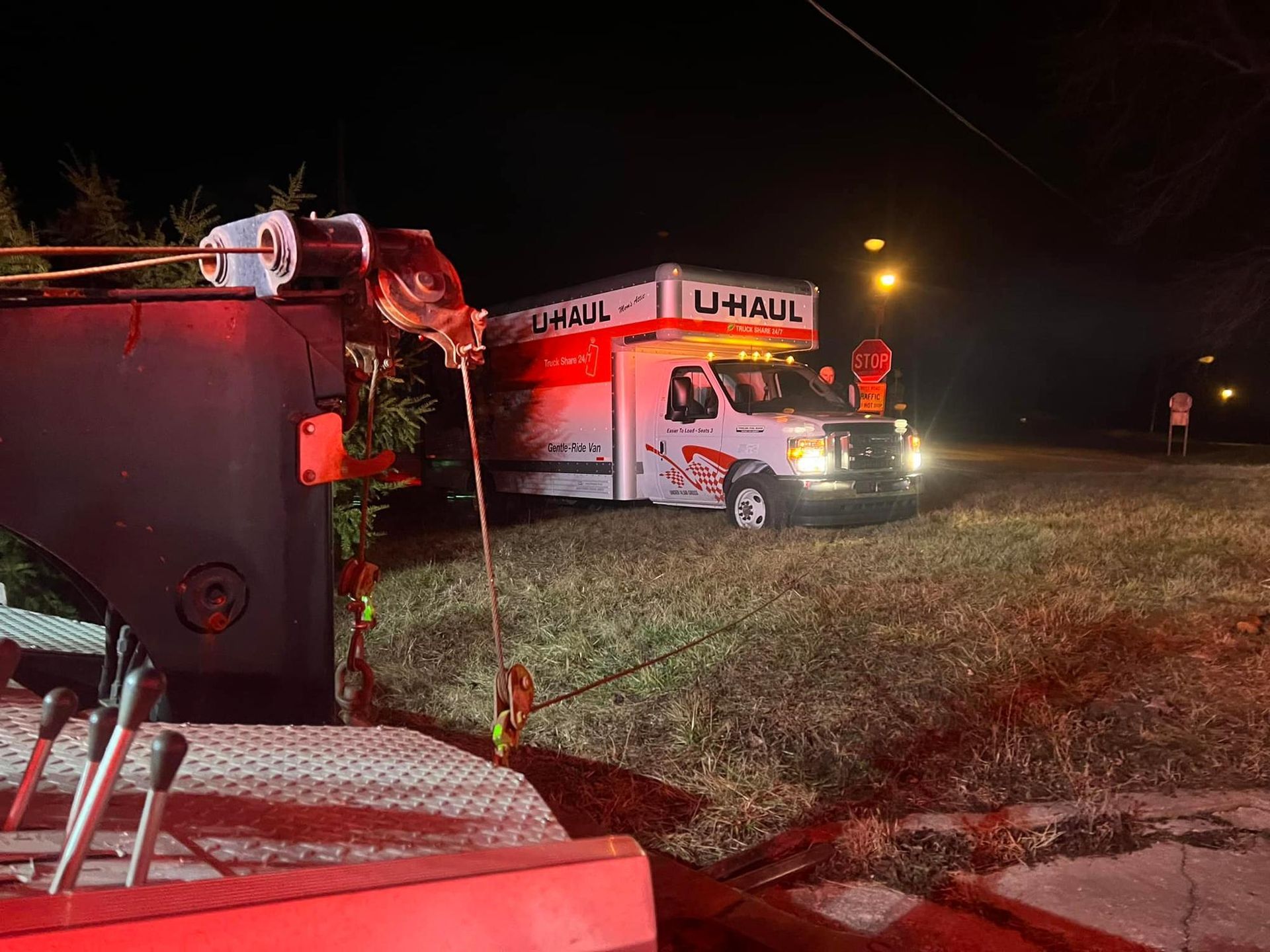 A uhaul truck is being towed by a tow truck at night.