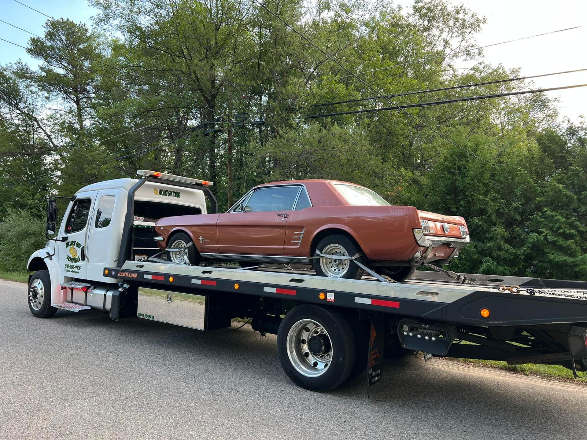 A tow truck is carrying a brown mustang on the back of it.