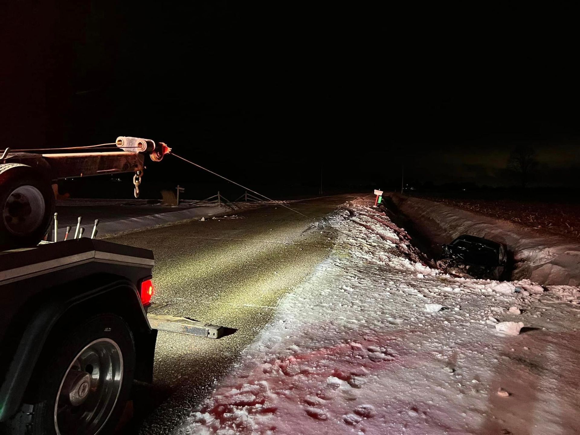A tow truck is pulling a car out of the snow at night.