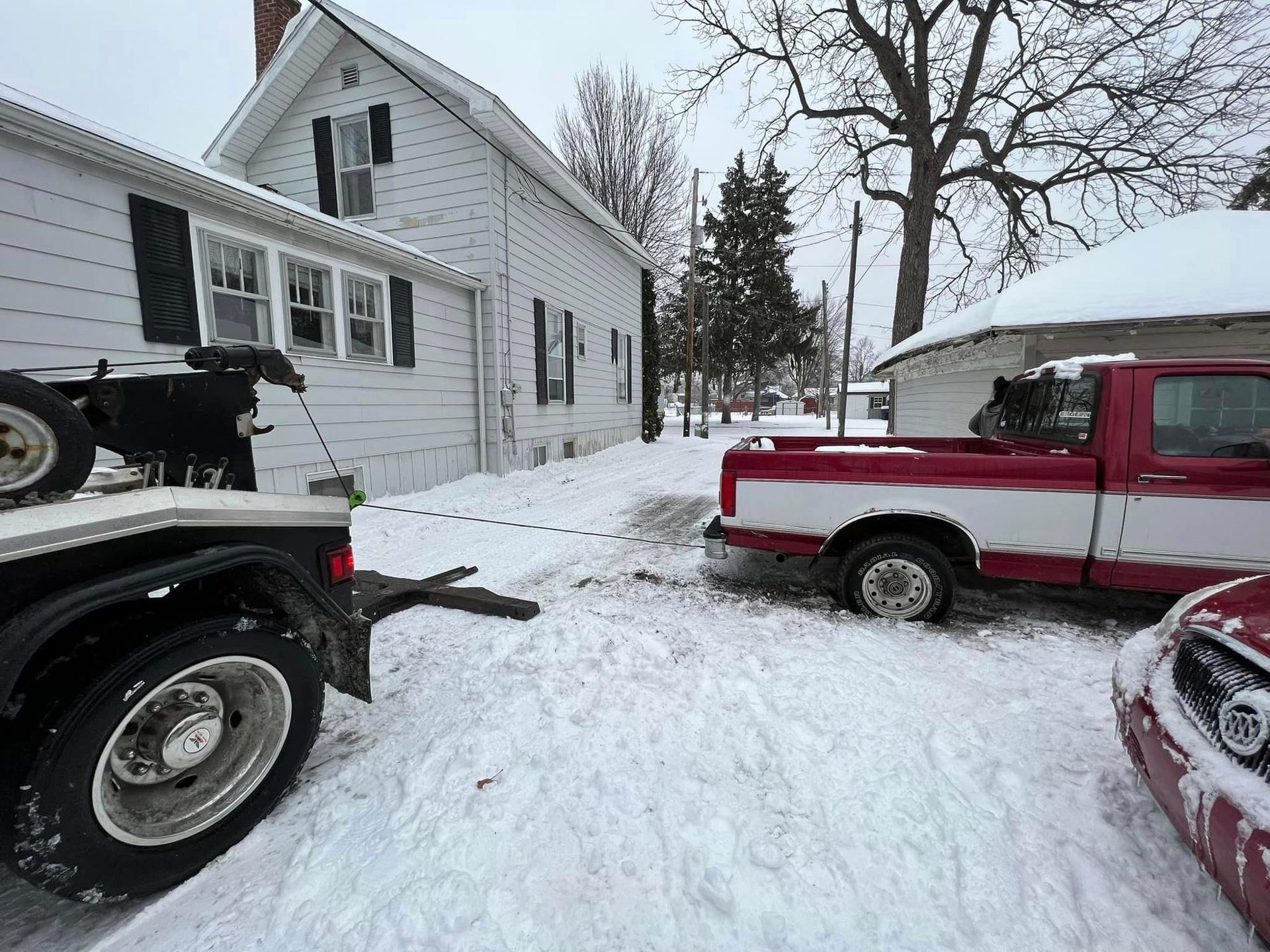 A red and white tow truck is towing a car in the snow.