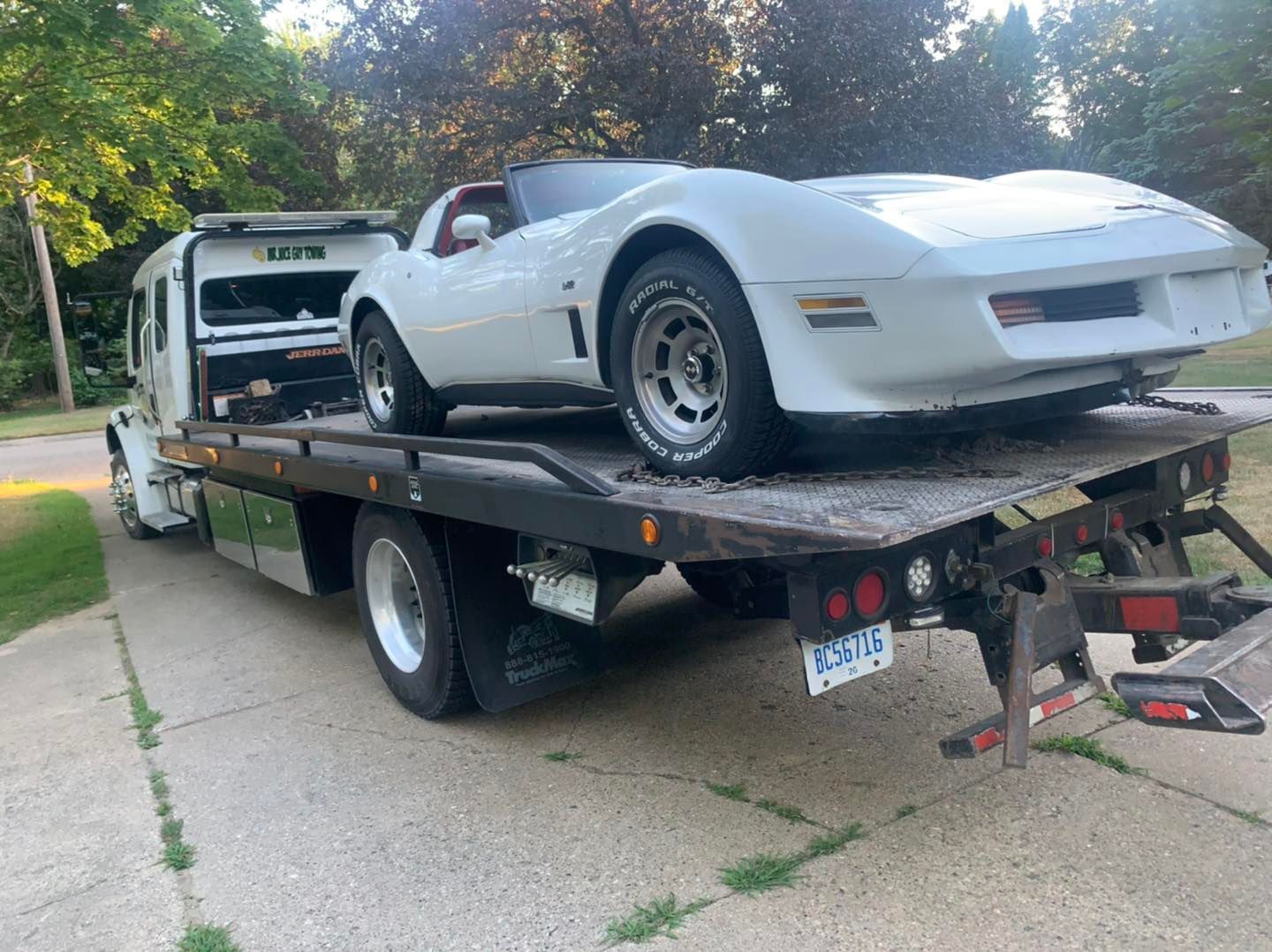 A white corvette is sitting on top of a tow truck.