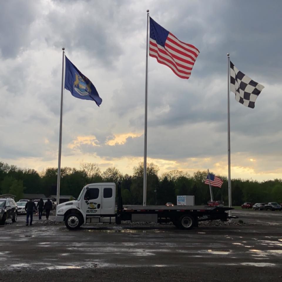 A tow truck is parked in a parking lot with flags flying in the background