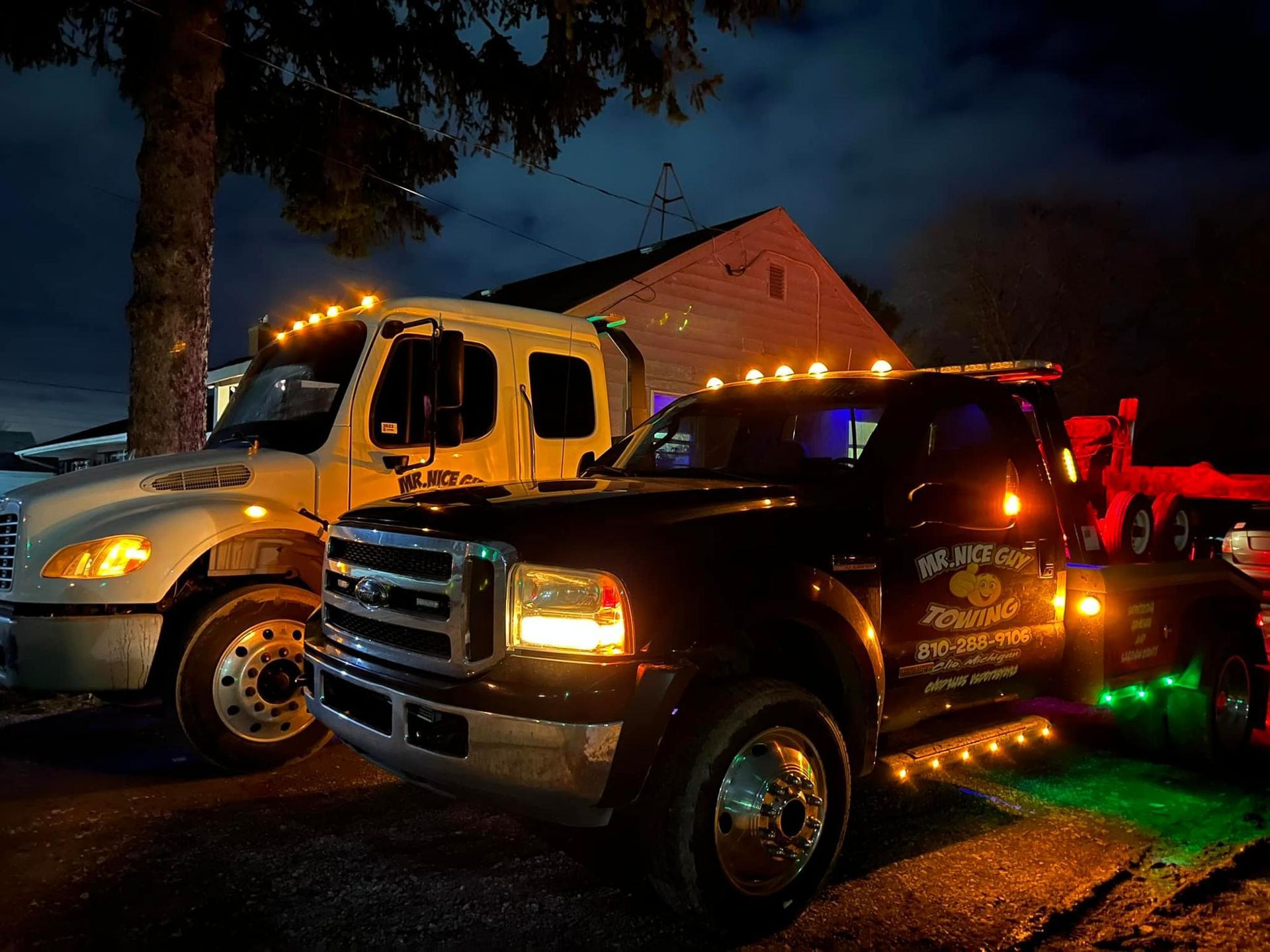 Two tow trucks are parked in front of a house at night.