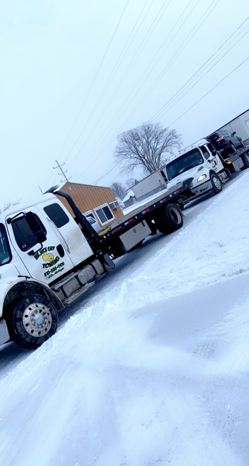 A tow truck is parked in the snow next to a house.