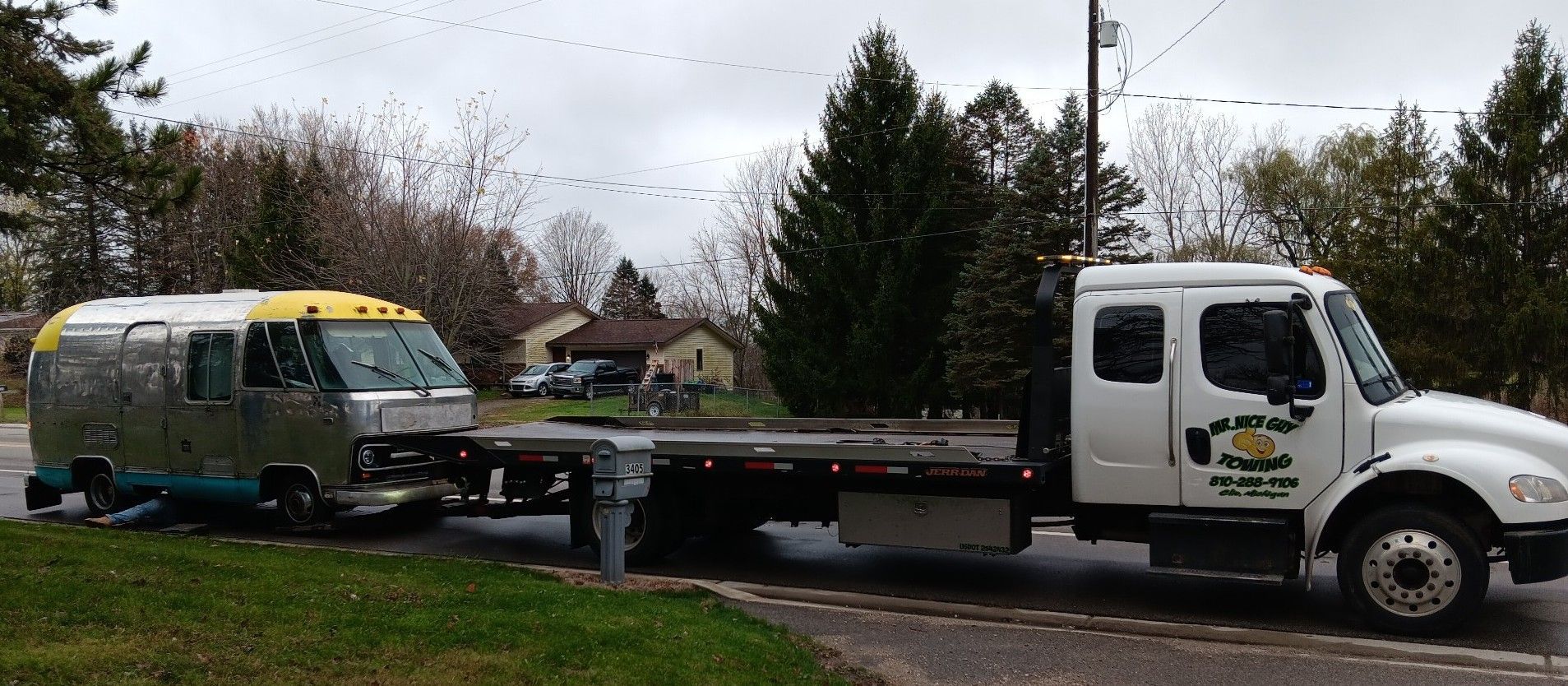 A tow truck is towing a trailer down a street.