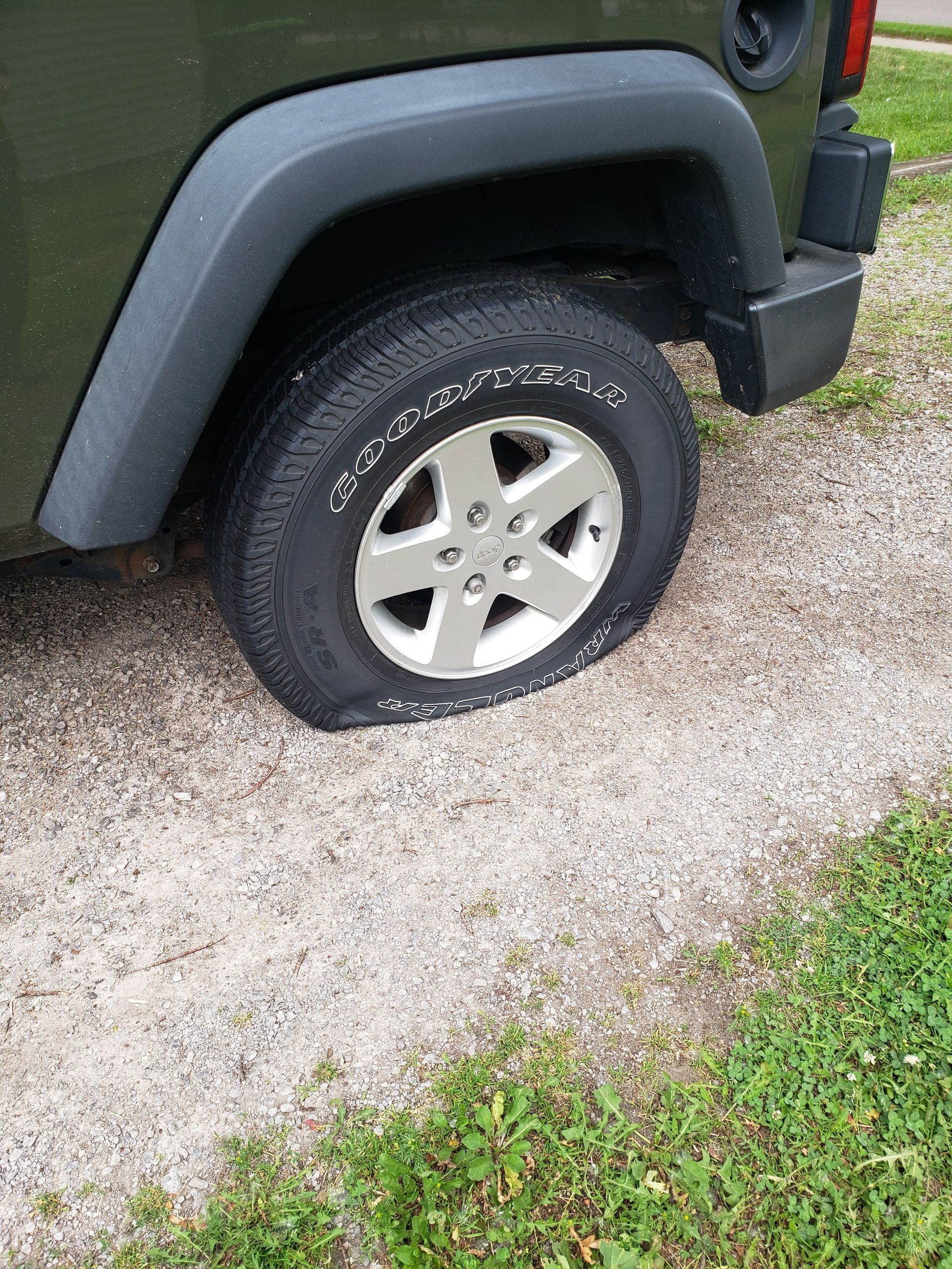 A jeep with a flat tire is parked in the grass.