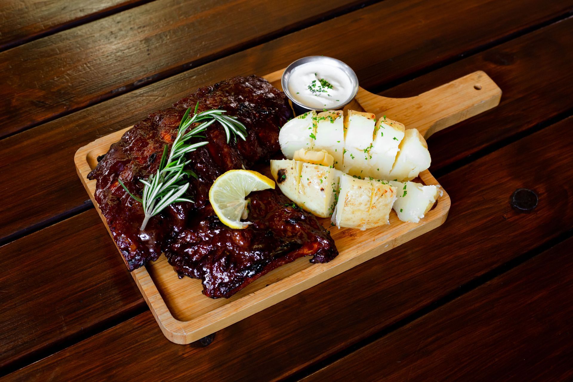 A wooden cutting board topped with meat and potatoes on a wooden table.