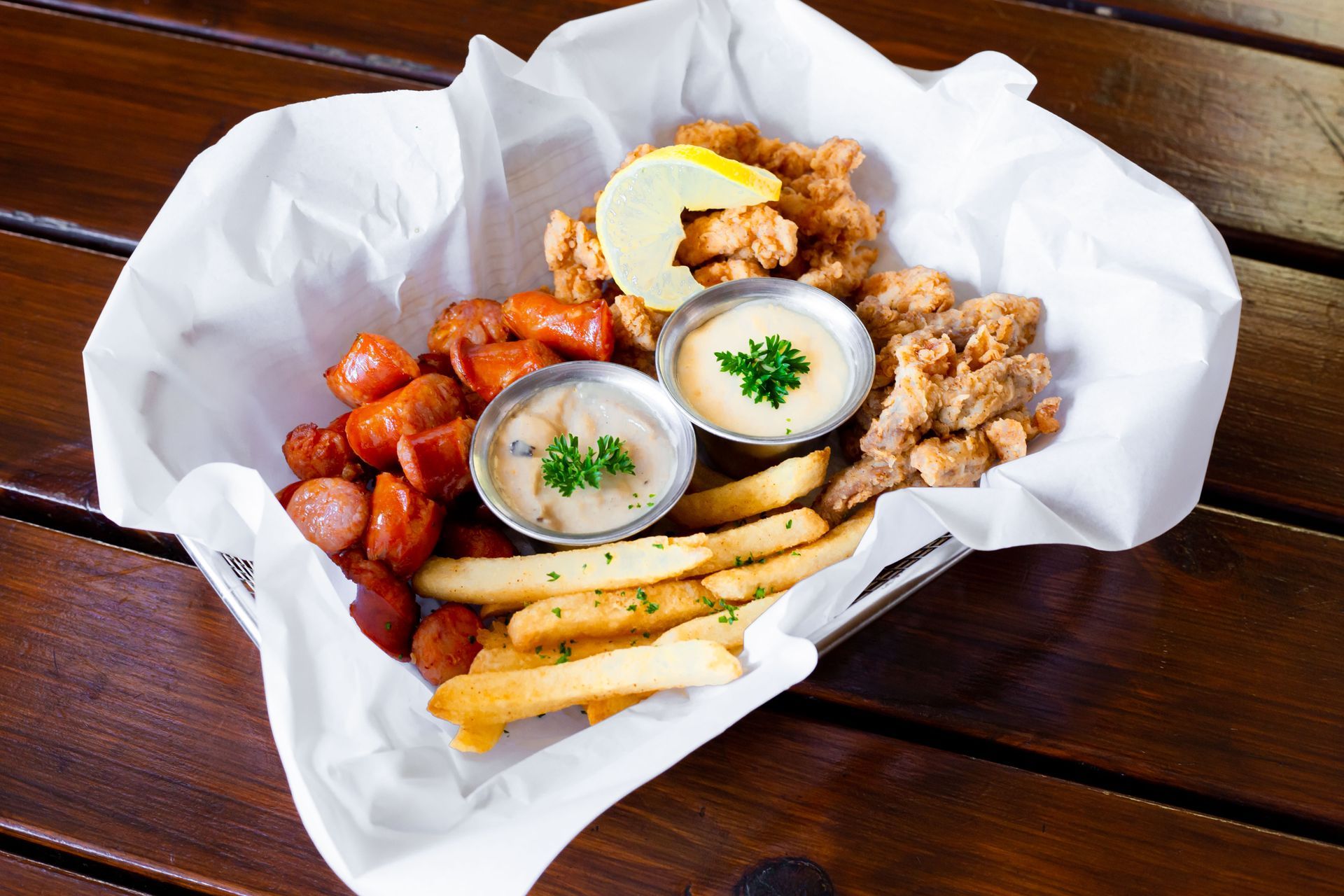 A basket of food with french fries , hot dogs , and shrimp on a wooden table.