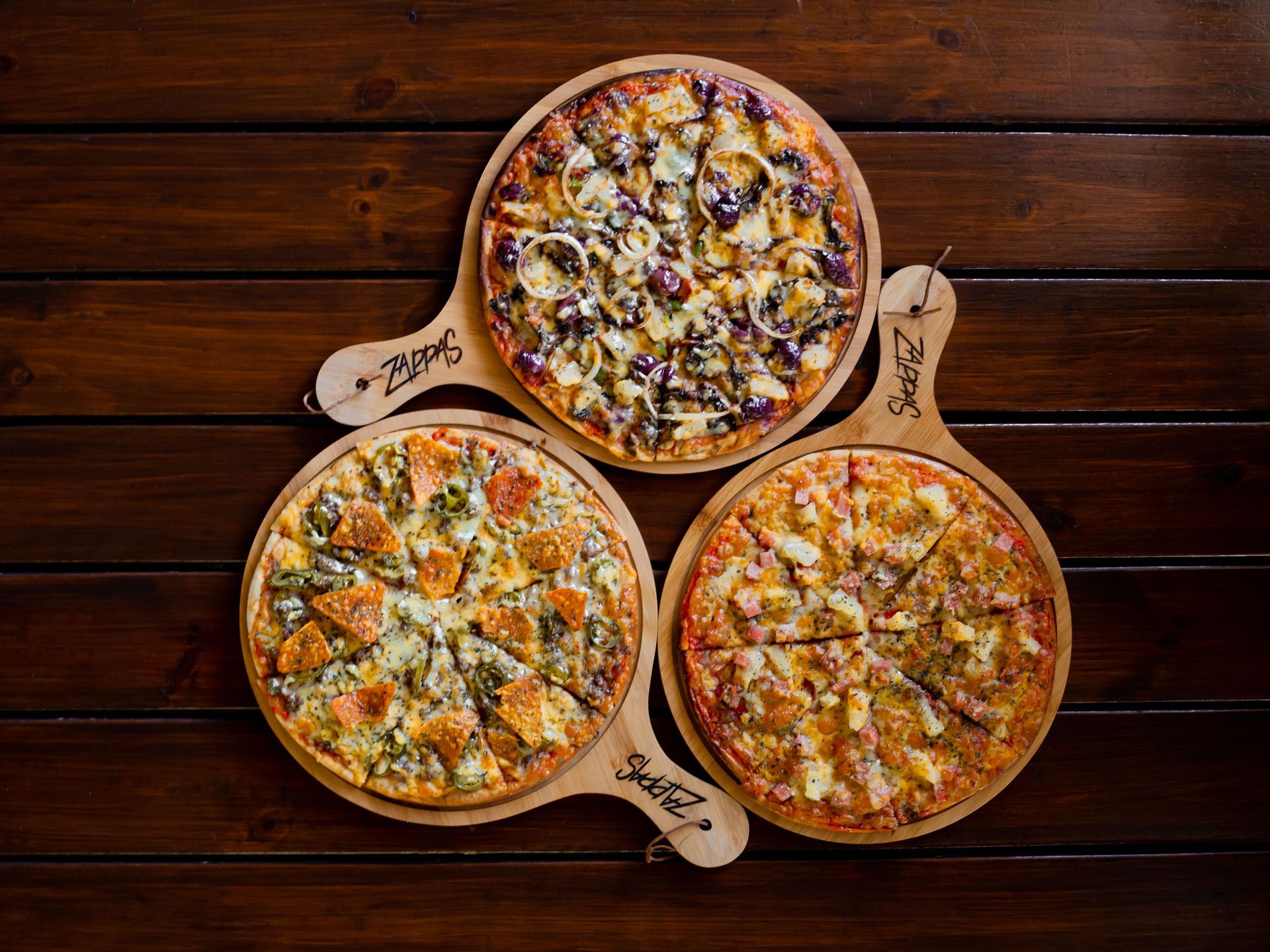 Three pizzas are sitting on wooden trays on a wooden table.