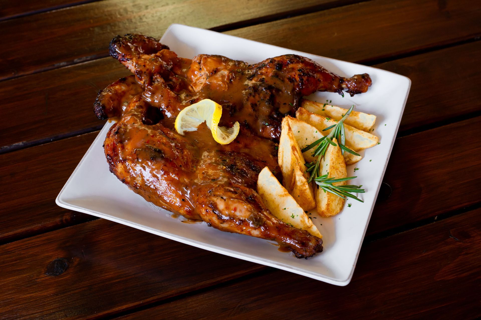 A white plate topped with chicken and french fries on a wooden table.