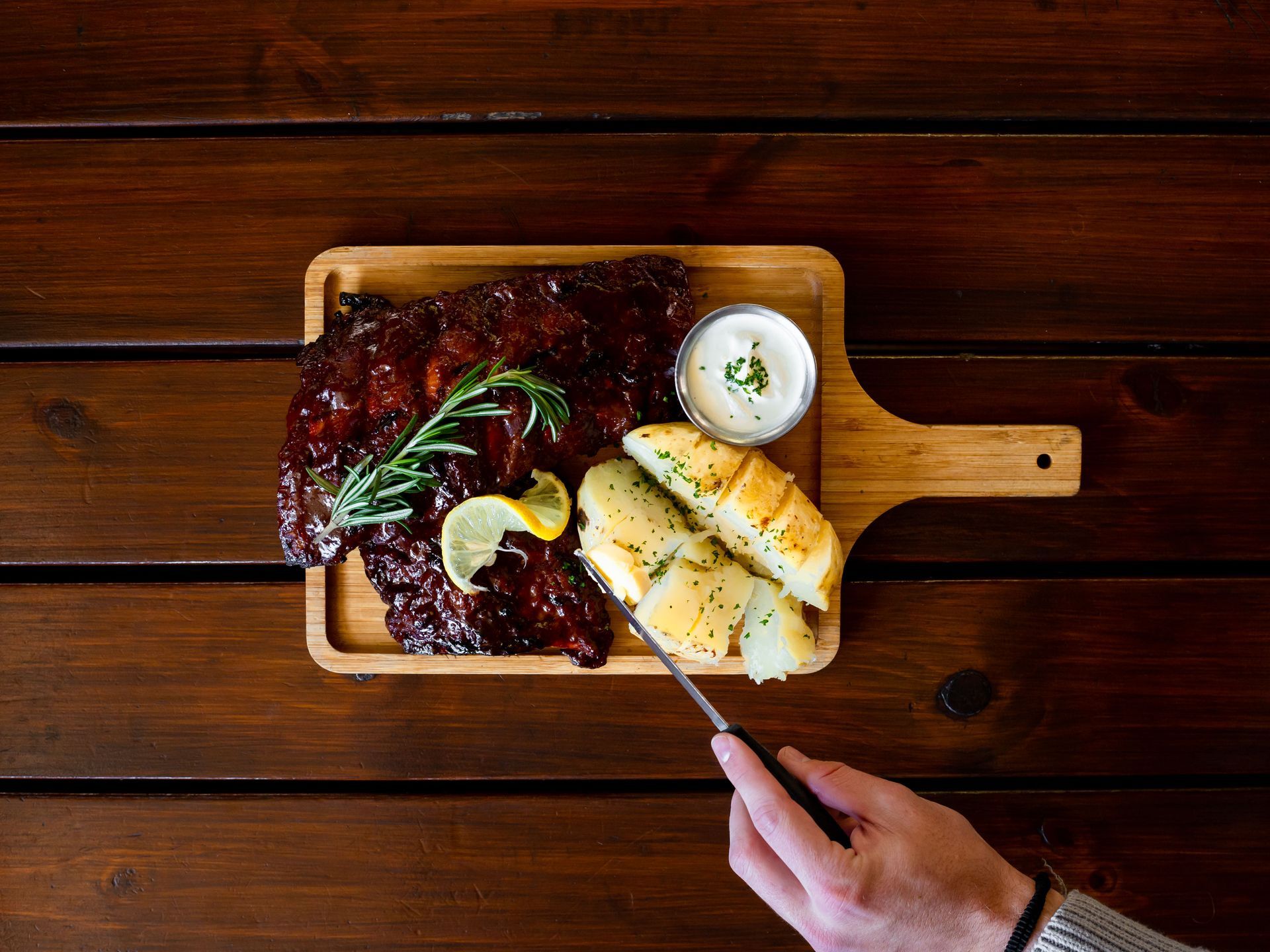A person is cutting a piece of meat on a wooden cutting board.