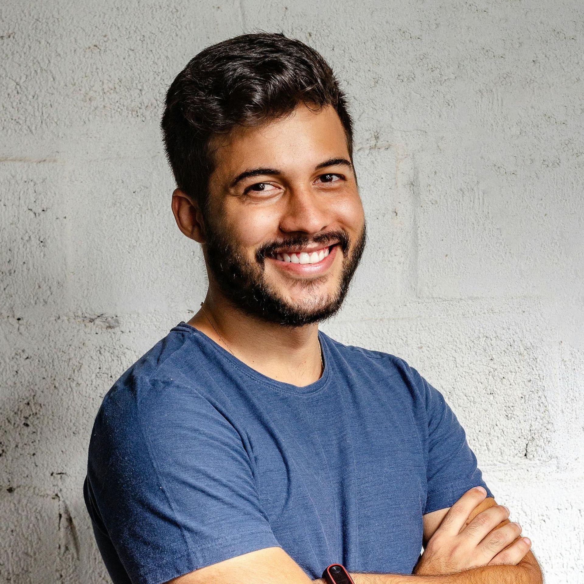 A man with a beard is wearing a blue shirt and smiling with his arms crossed.