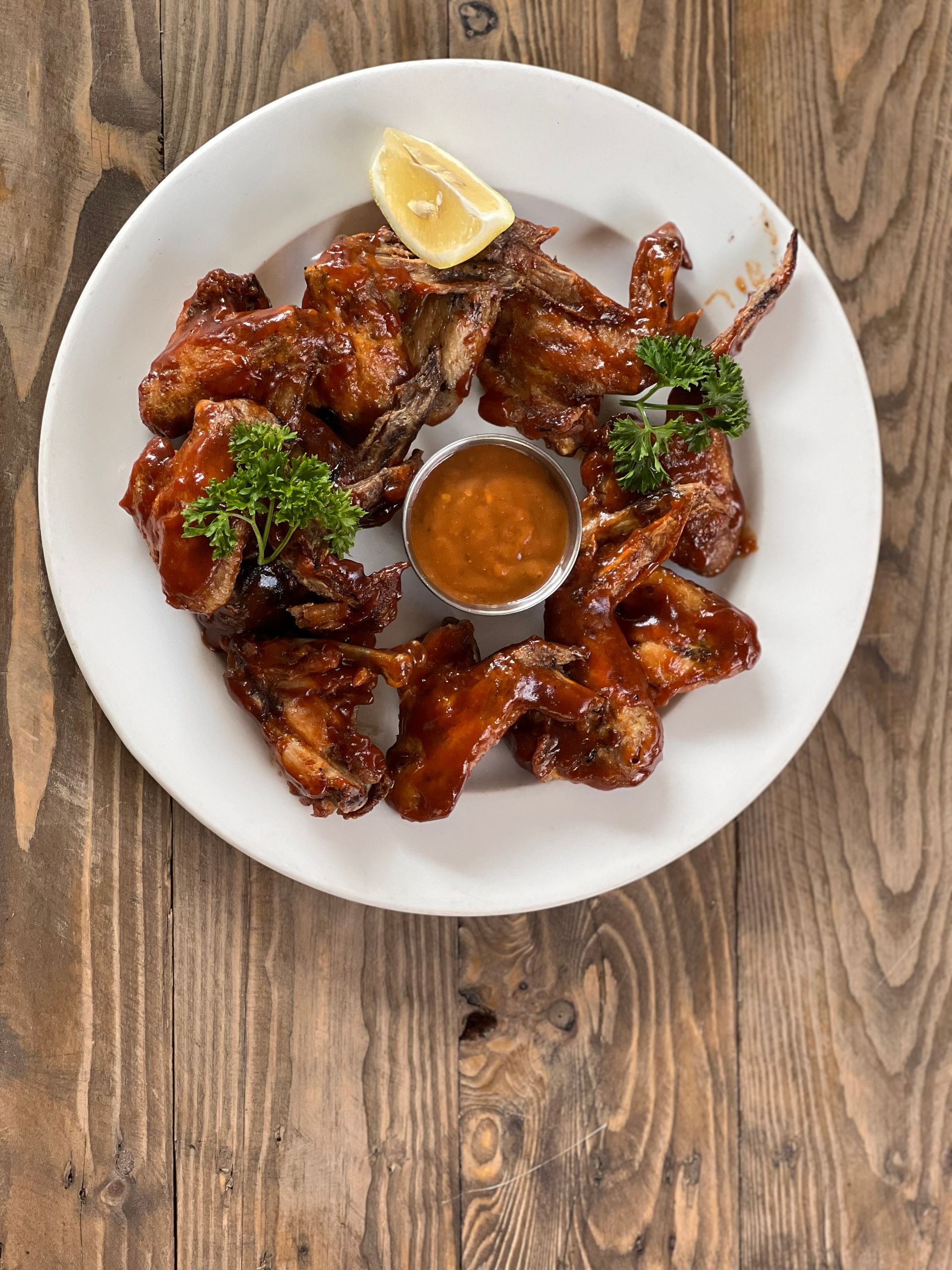 A white plate topped with chicken wings and sauce on a wooden table.
