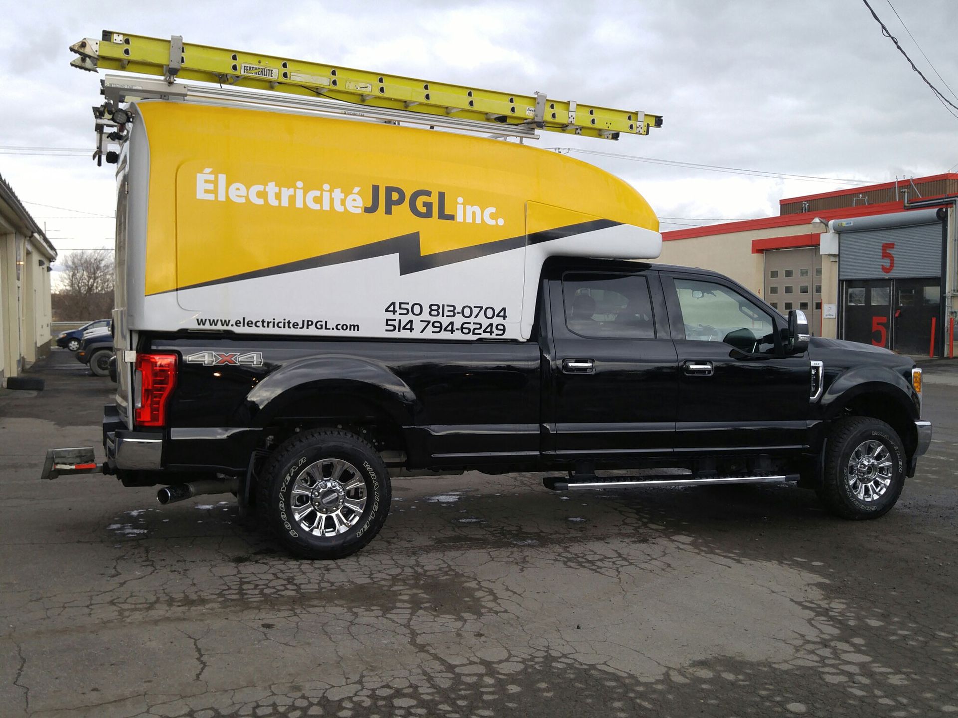 Un camion noir avec un auvent jaune qui dit electricite jpg inc.