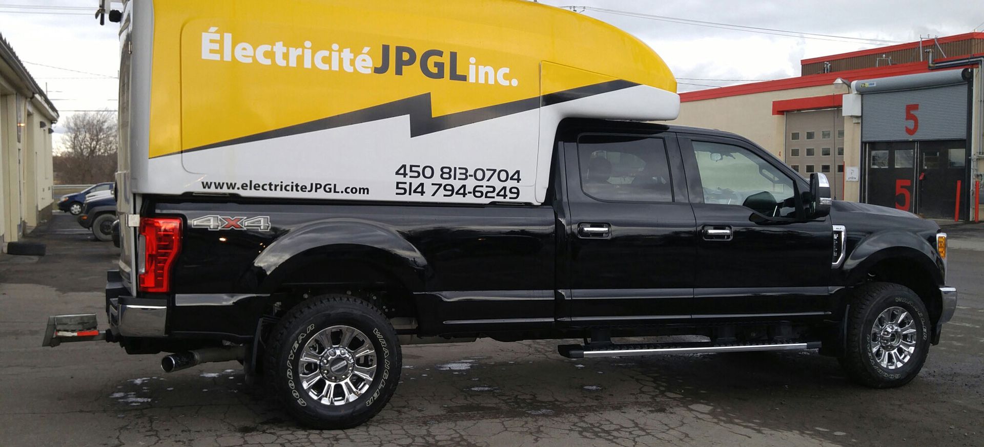 Un camion noir avec un auvent jaune est garé devant un immeuble.