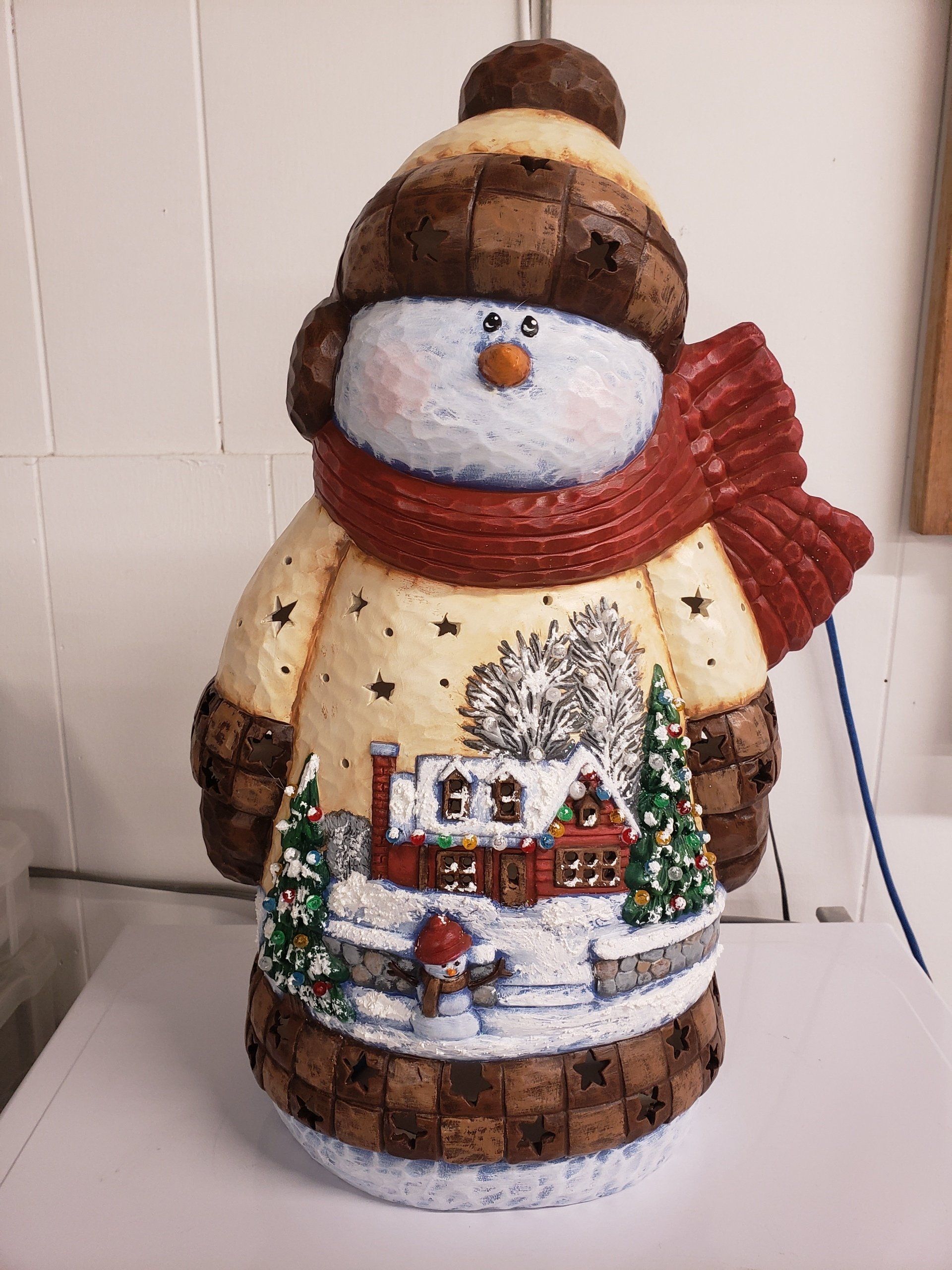 A snowman with a scarf around his neck is sitting on a washing machine.