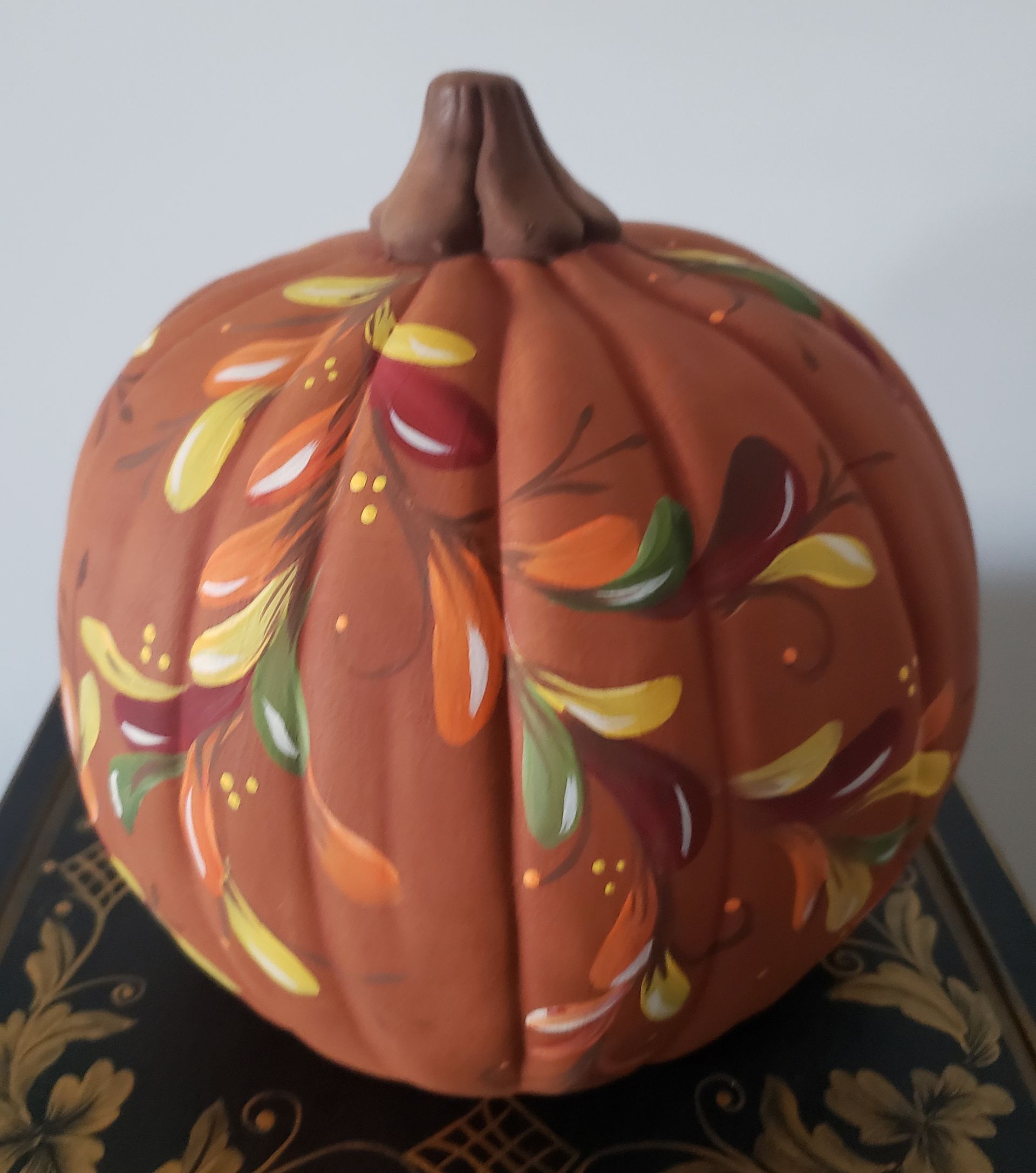 A pumpkin with leaves painted on it sits on a table
