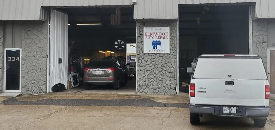 A car repair shop with a bus inside, other vehicles outside. Sunny day.
