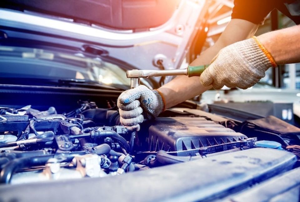 Mechanic using wrench to work on a car engine in a garage, wearing gloves.