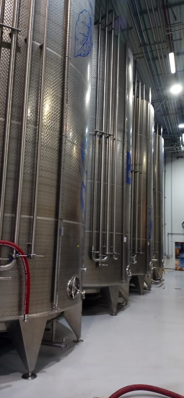 Tanques de fermentación de acero inoxidable en una bodega, vistos desde un ángulo en un almacén.