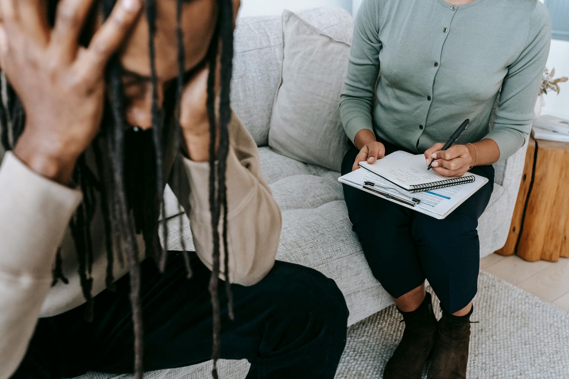 Person with dreadlocks in therapy session, head in hands, while therapist takes notes.