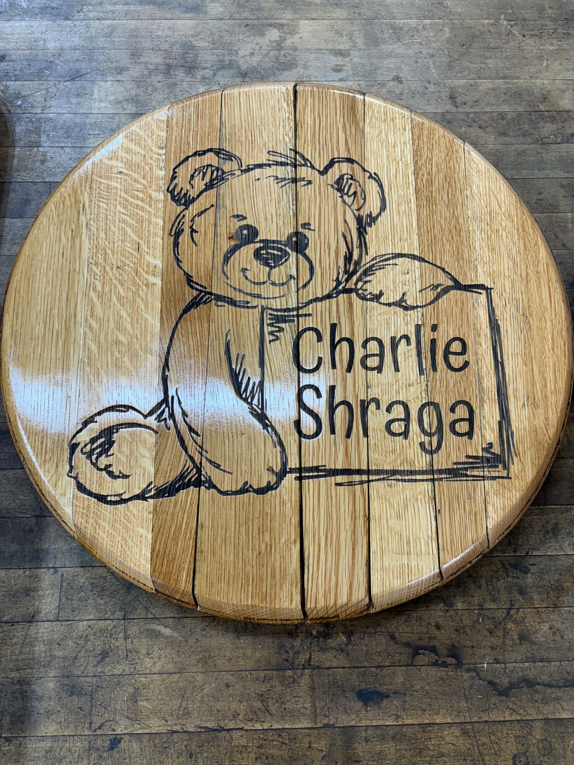 A wooden cutting board with a teddy bear and the name charlie shraga on it.