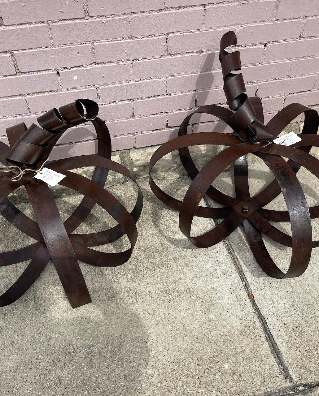 Two metal sculptures are sitting on a sidewalk in front of a brick wall