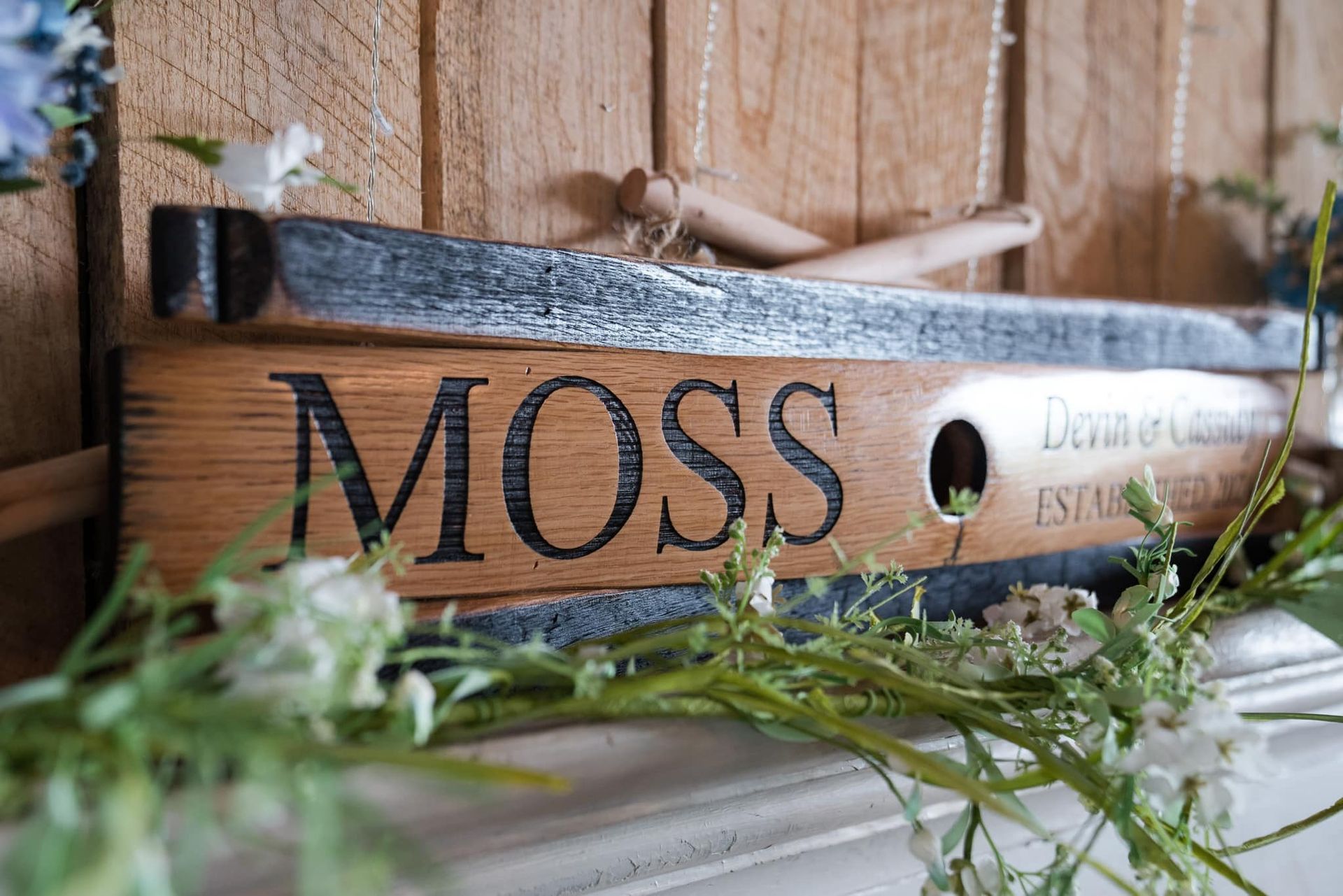 A wooden sign that says moss is sitting on a mantle next to flowers.