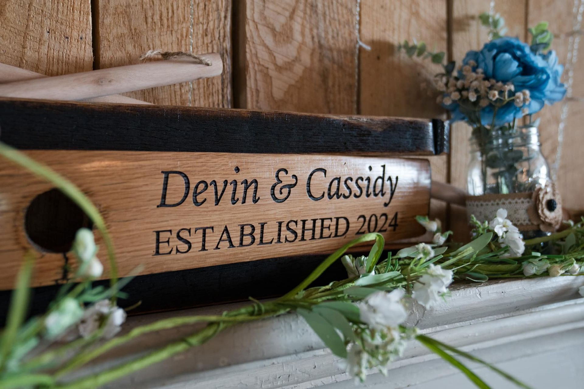 A wooden box with the names devin and cassidy written on it is sitting on a mantle next to flowers.