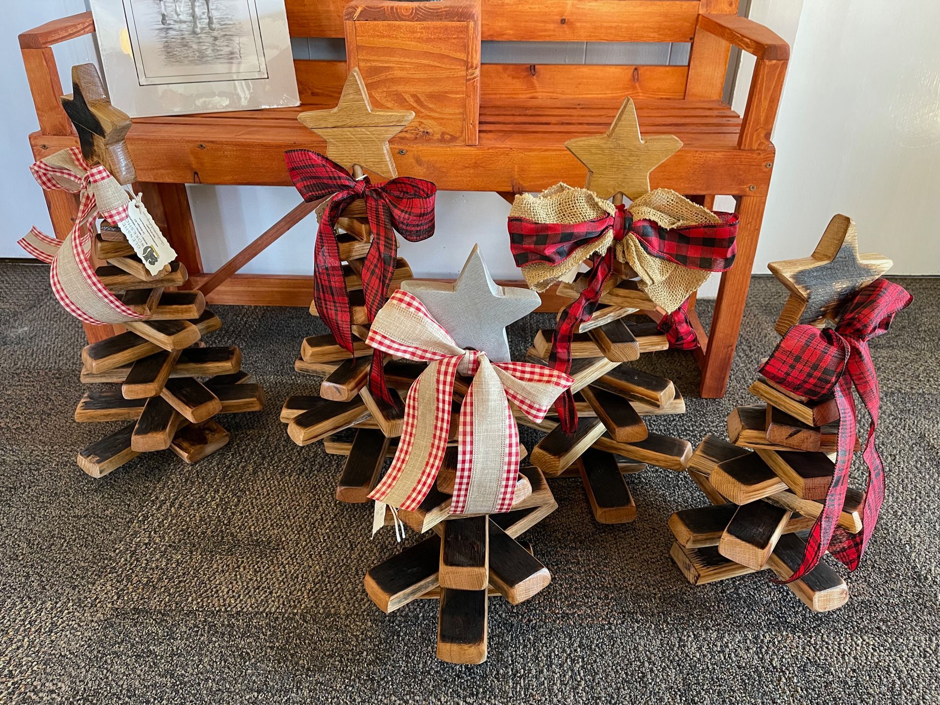 Three wooden christmas trees are sitting next to a wooden bench.