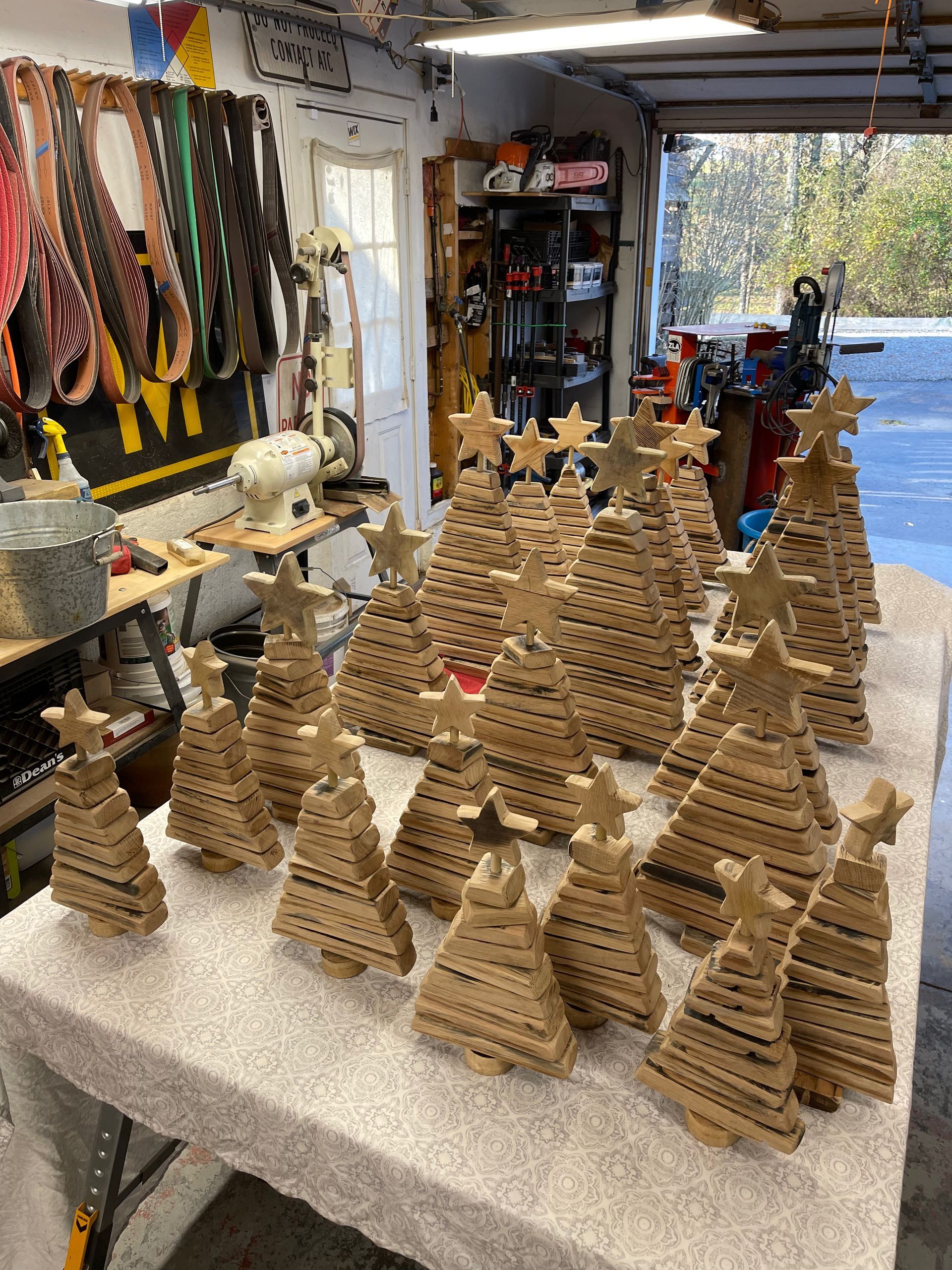 A bunch of wooden christmas trees are sitting on a table in a garage.
