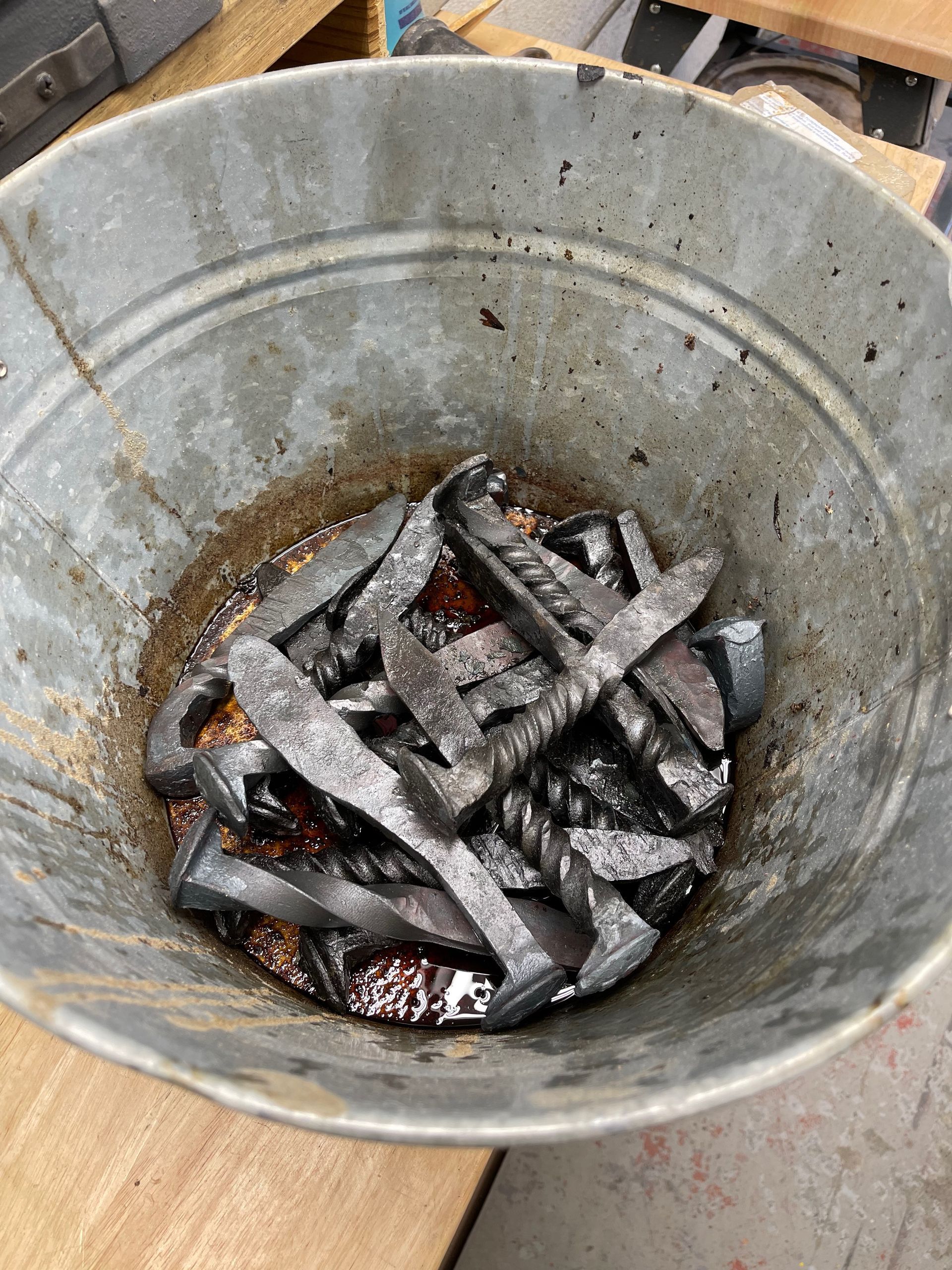 A metal bucket filled with nails is sitting on a wooden table.