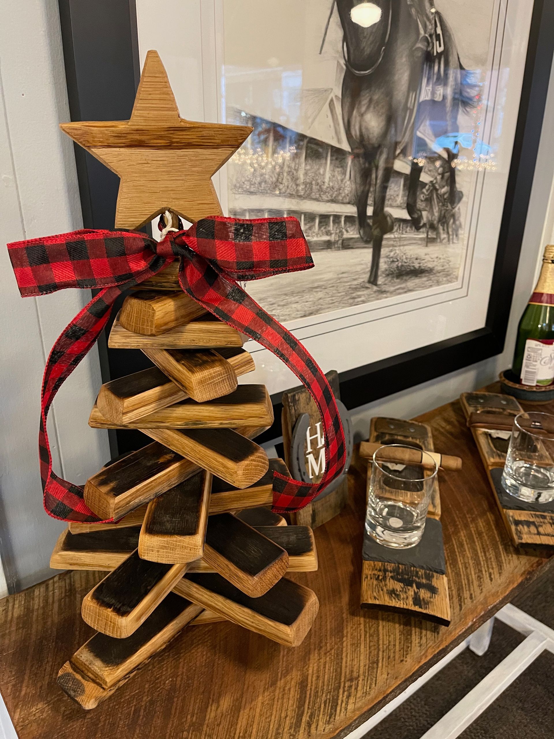 A wooden christmas tree is sitting on top of a wooden table next to a picture of a horse.