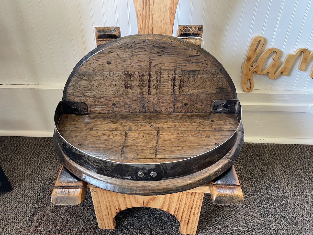A wooden chair made out of a barrel is sitting on a carpeted floor.
