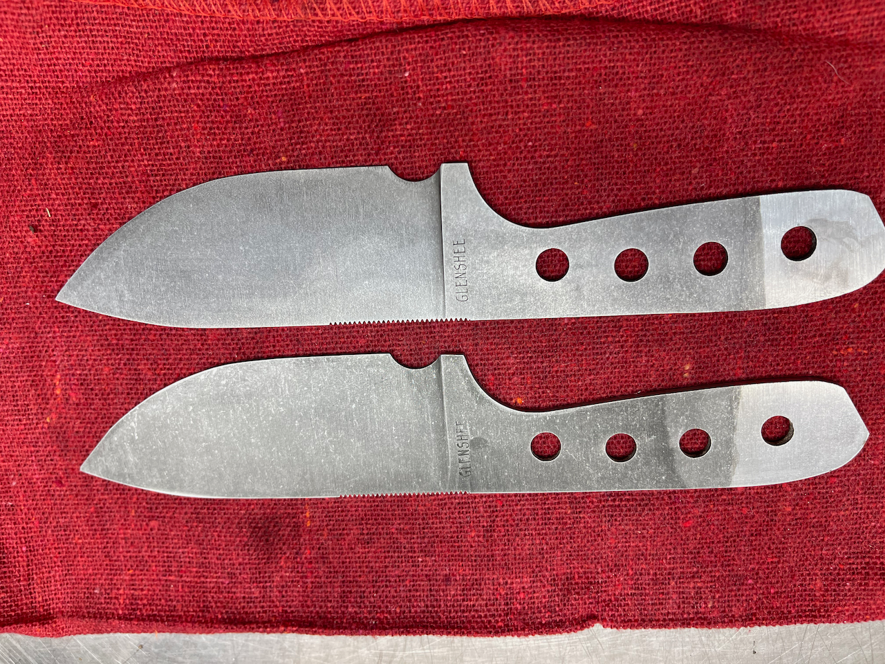 Two knives are laying on a red cloth