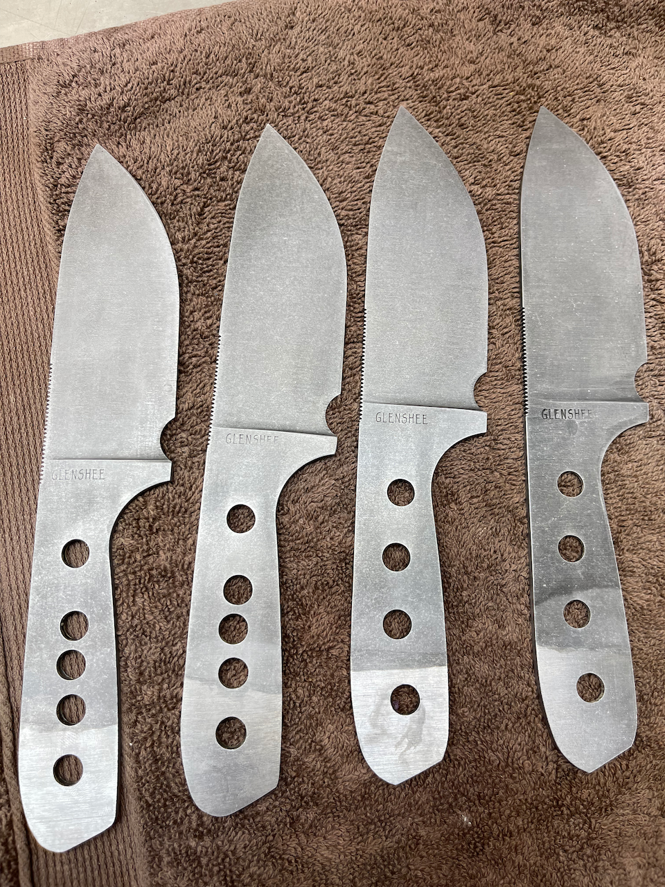 Four knives are lined up on a brown towel.