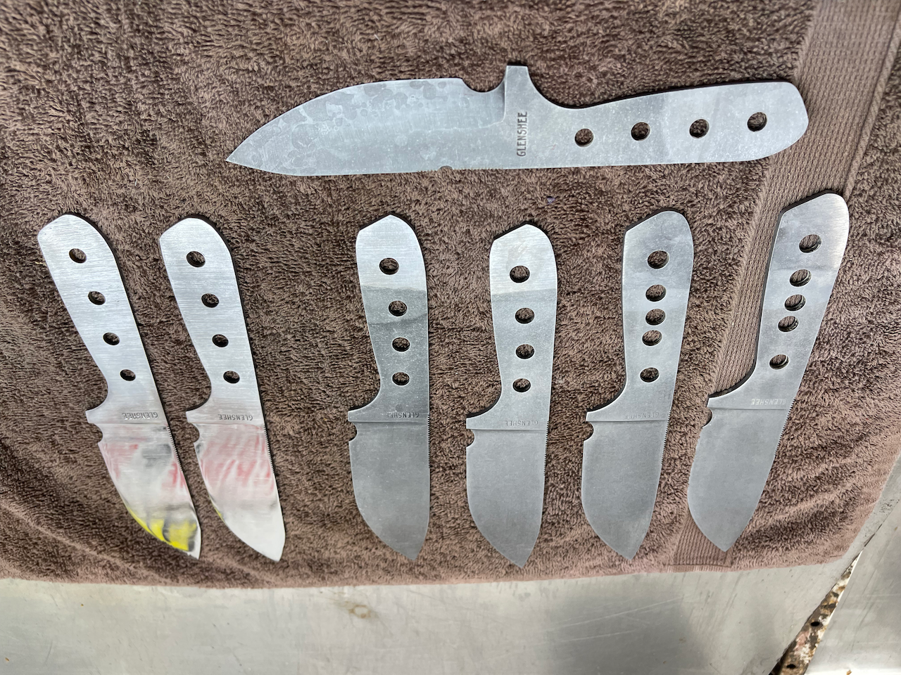 A bunch of knives are laying on a brown towel