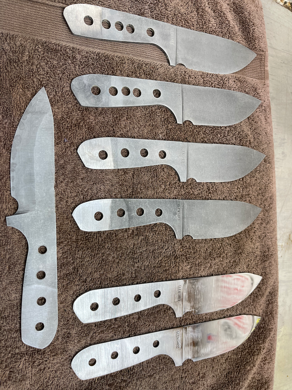 A bunch of knives are laying on a brown towel.