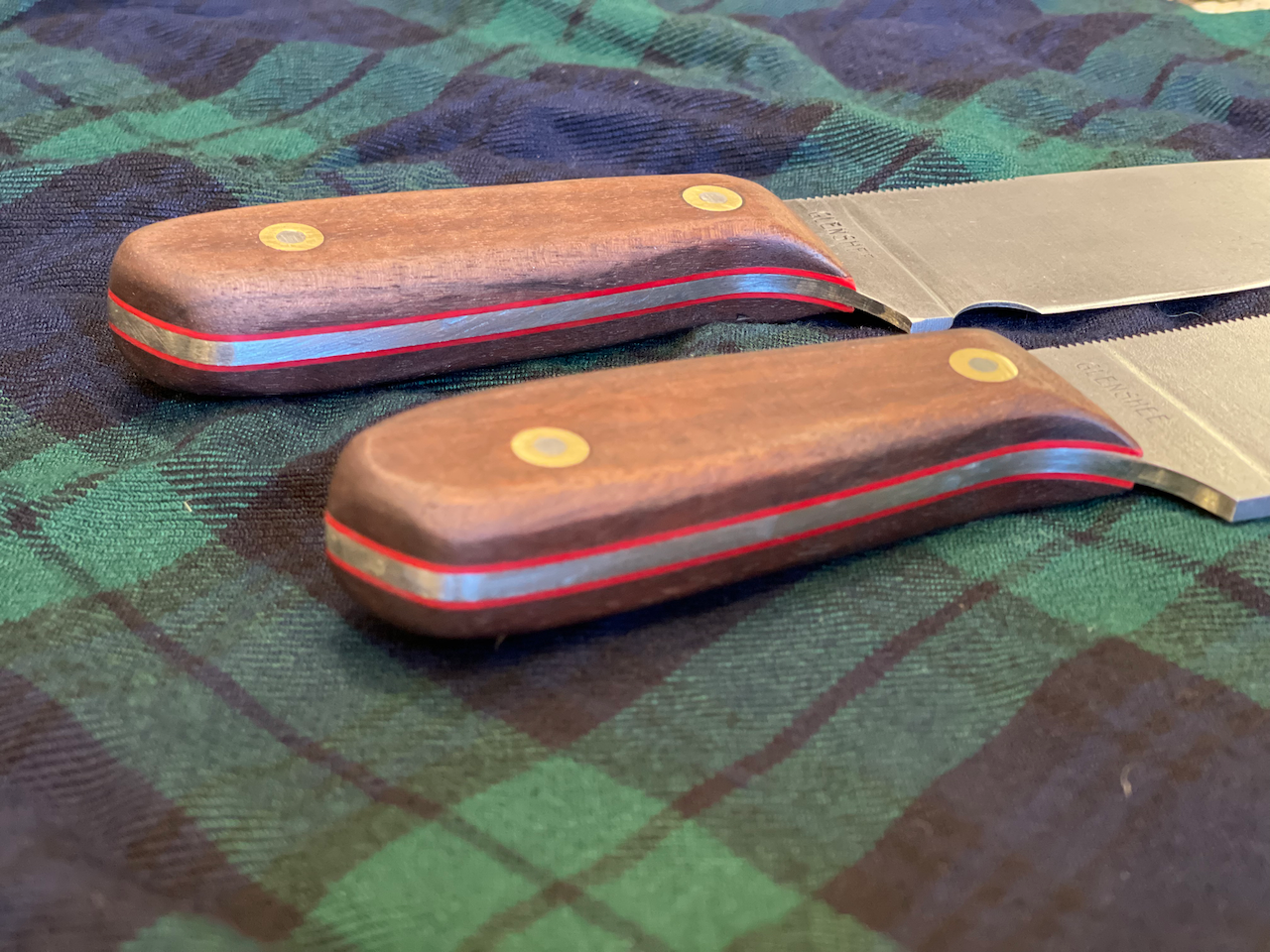 Two knives with wooden handles are sitting on a plaid cloth.