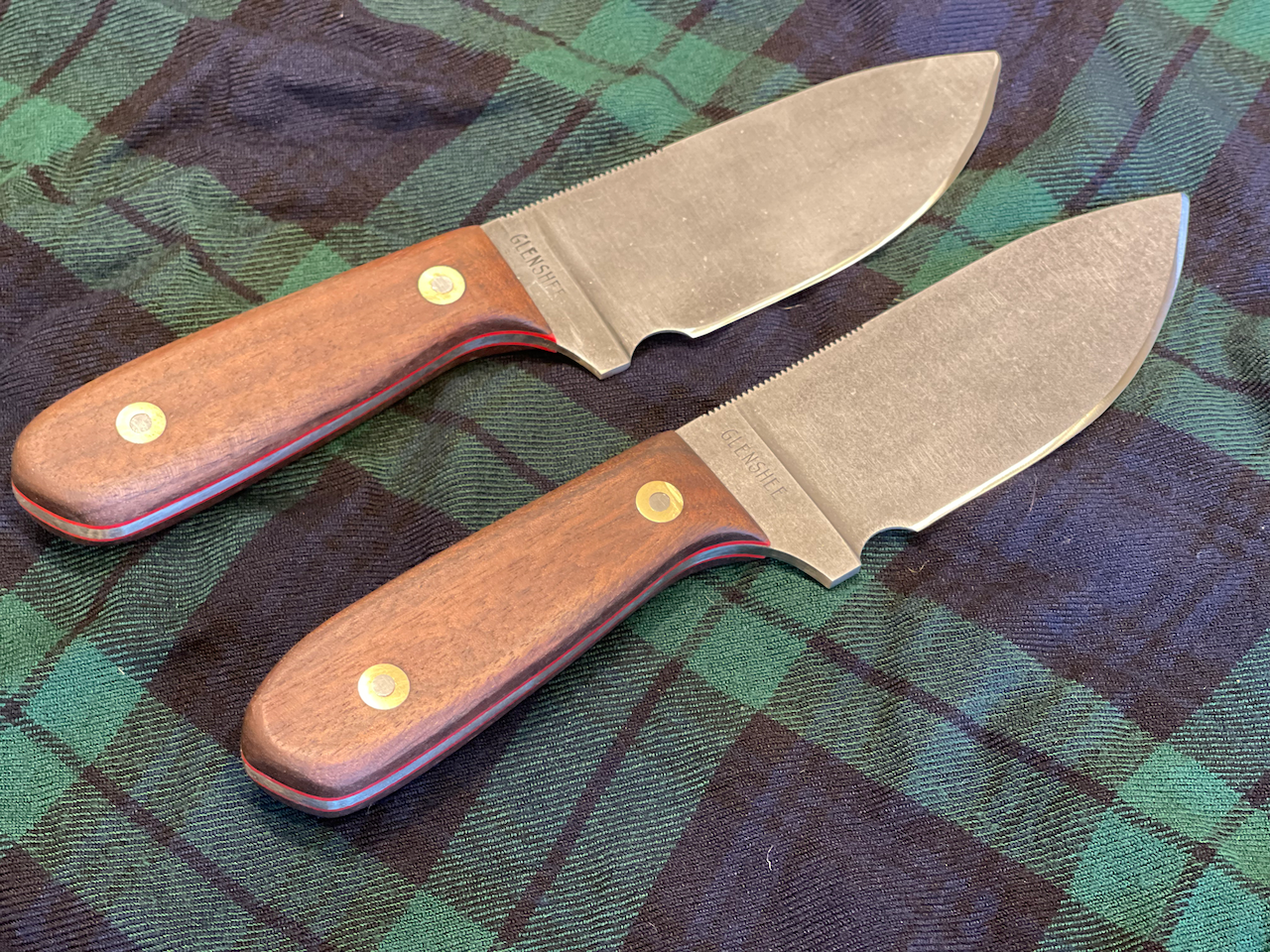 Two knives with wooden handles are sitting on a plaid cloth.
